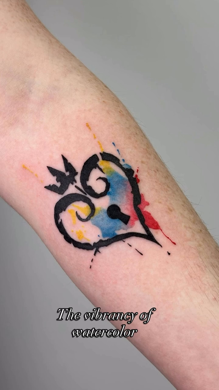 Heart with keyhole and watercolor splashes watercolor tattoo on the forearm by Mandy Kaur