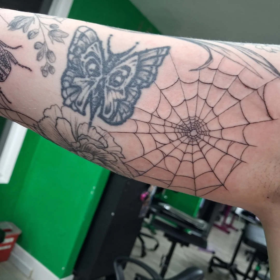 Butterfly and spider web black and grey tattoo on the forearm by James Ostler