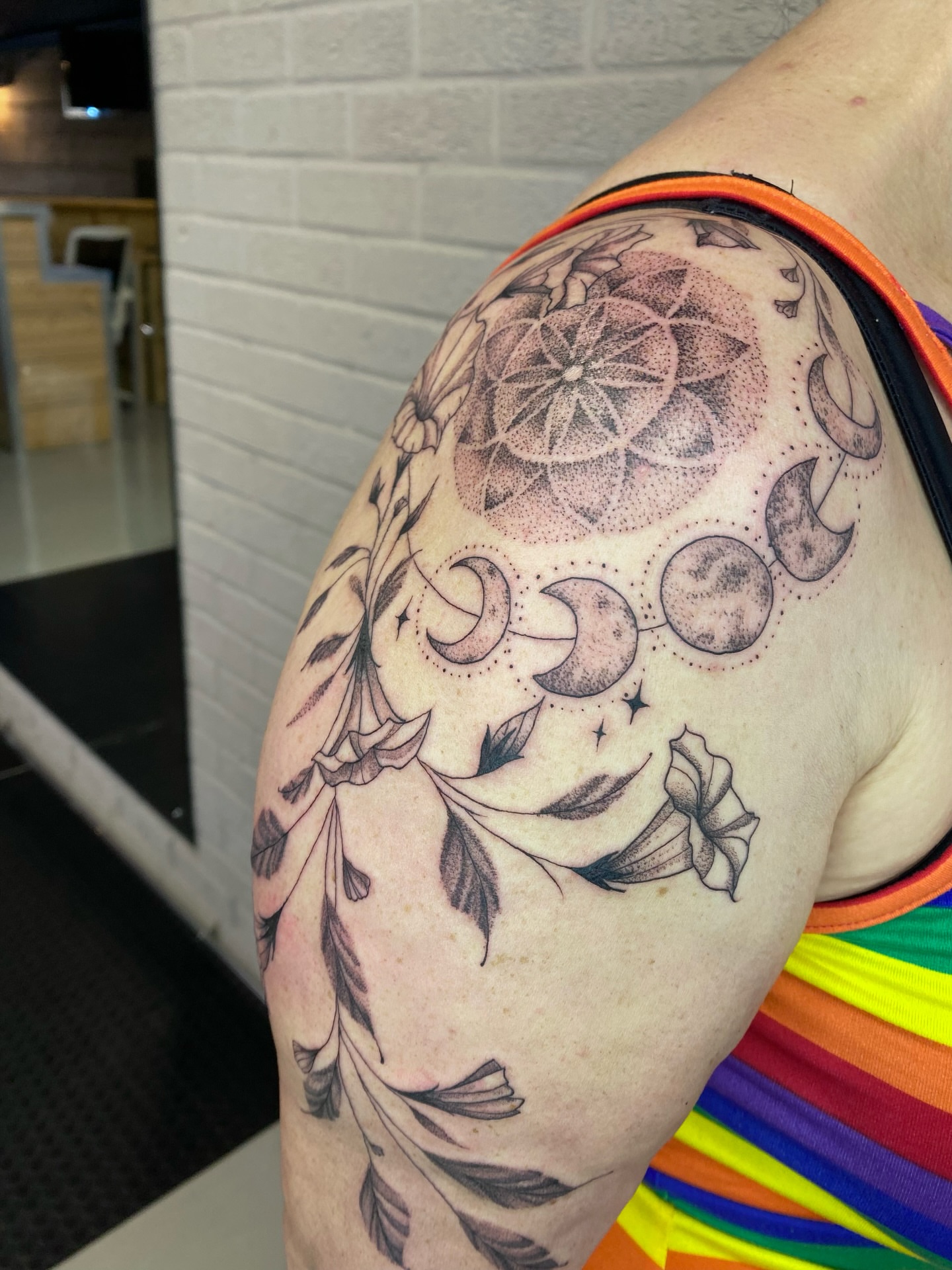 Moon phases and floral dotwork tattoo on the shoulder by Ellena Reggiani