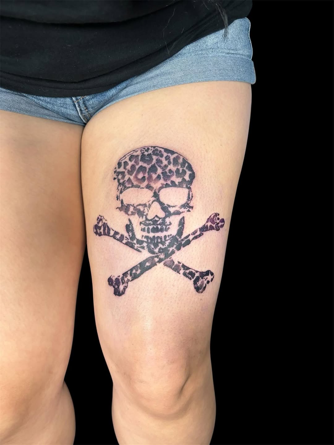 Skull and crossbones with leopard print realism tattoo on the thigh by @inkwitatlas