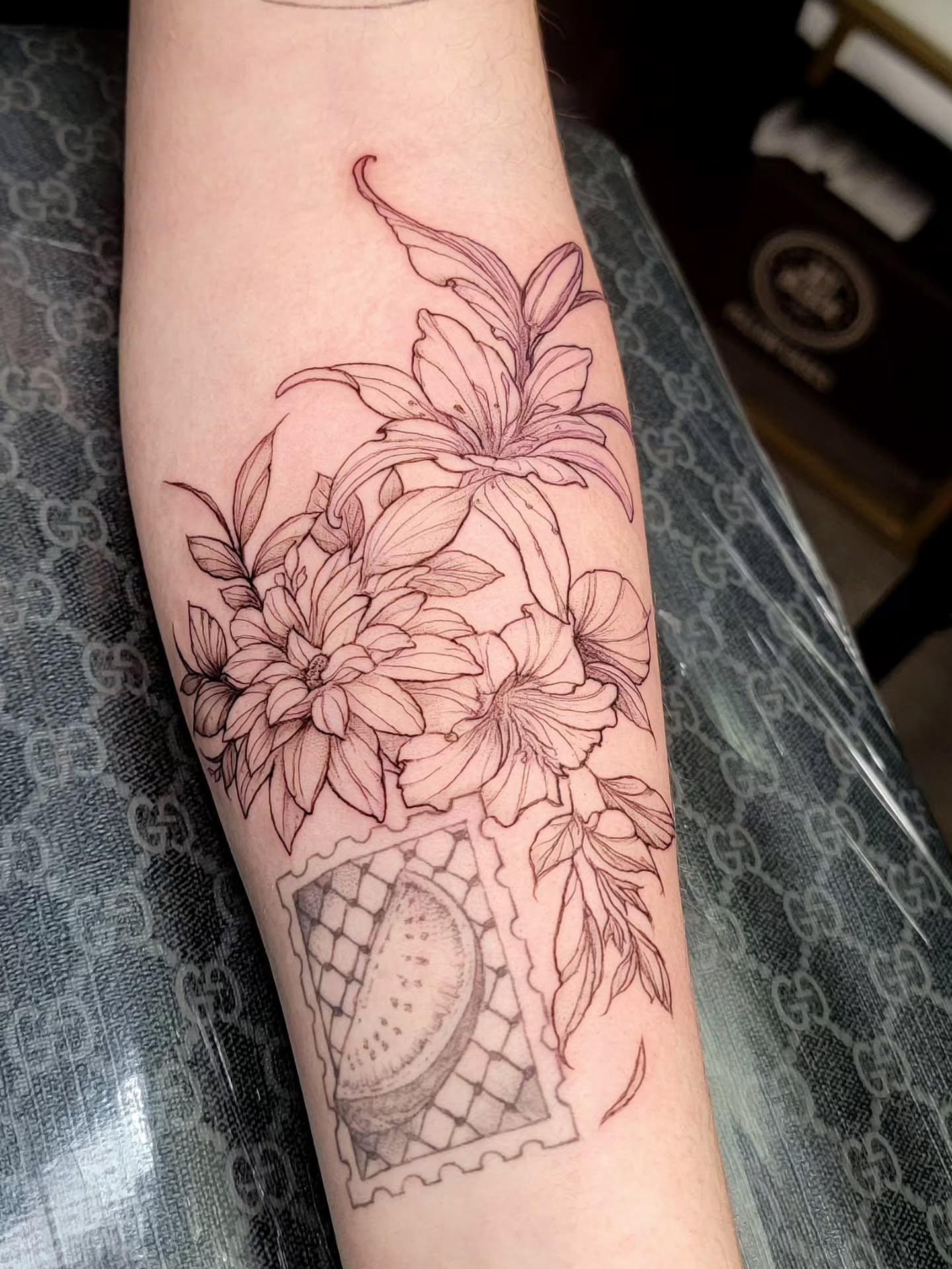 Flowers and postage stamp black and grey tattoo on the forearm by Nathan Harkins-Oberbeck