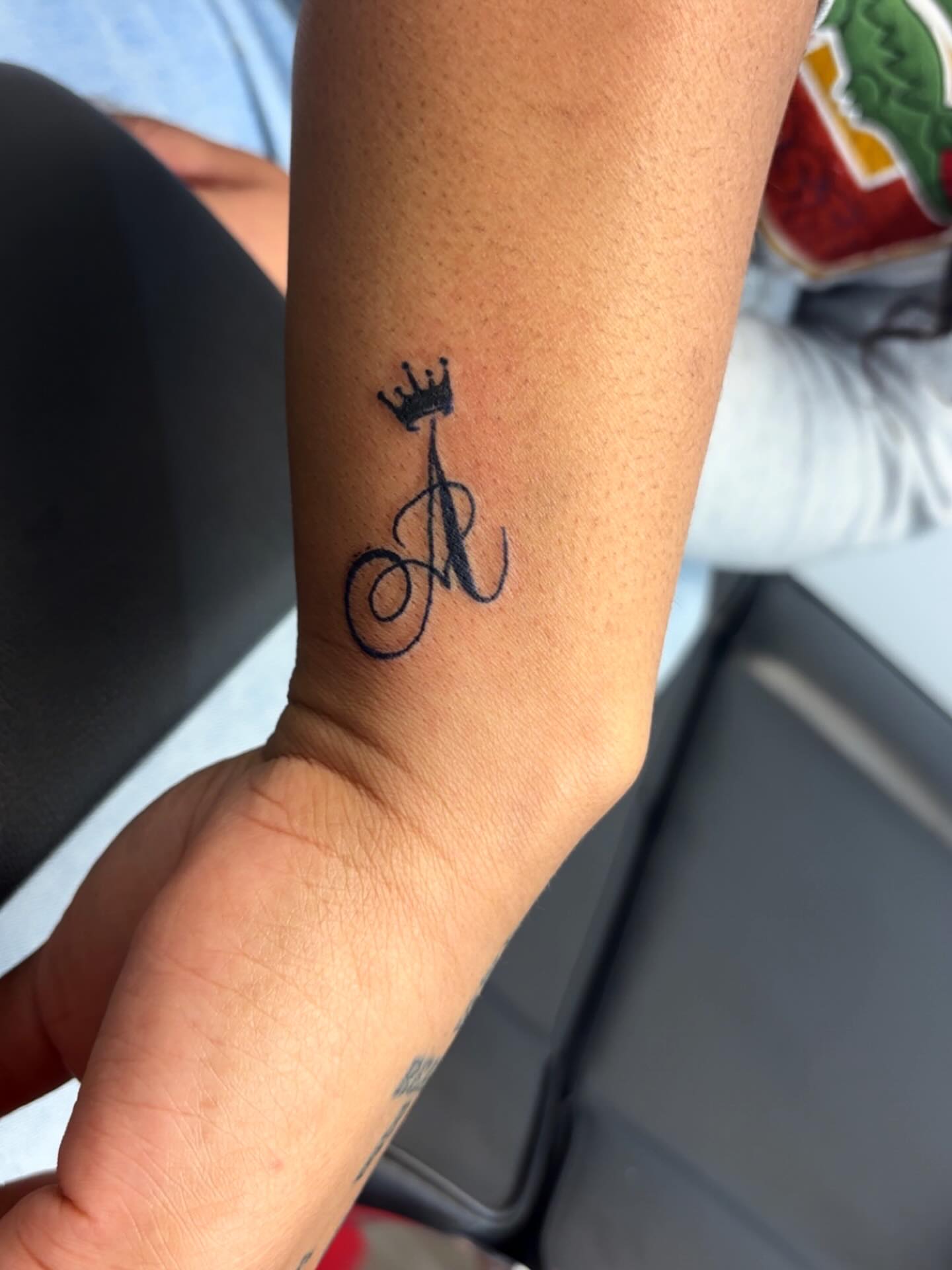Initial with crown lettering script tattoo on the forearm by Syneca Wilson, Acton, Massachusetts