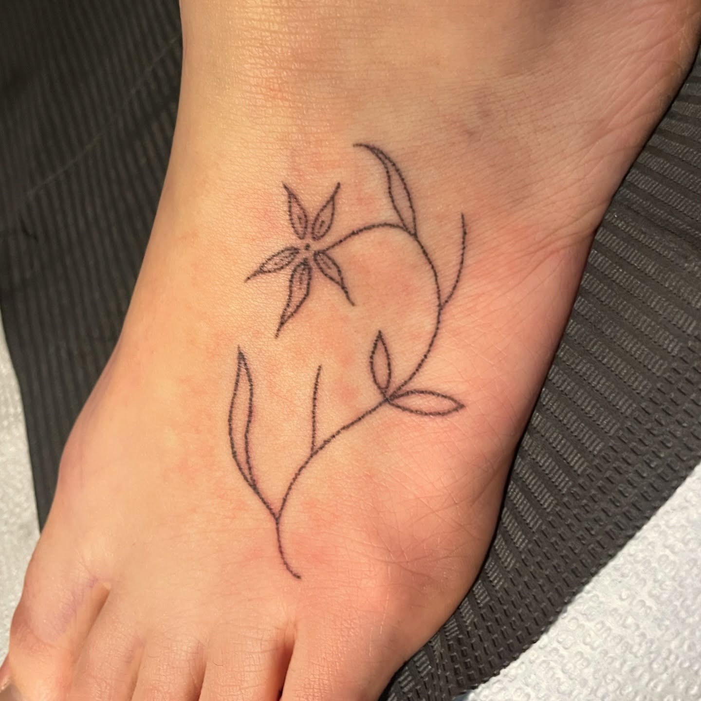 Flower and vine minimalist tattoo on the foot by Roe