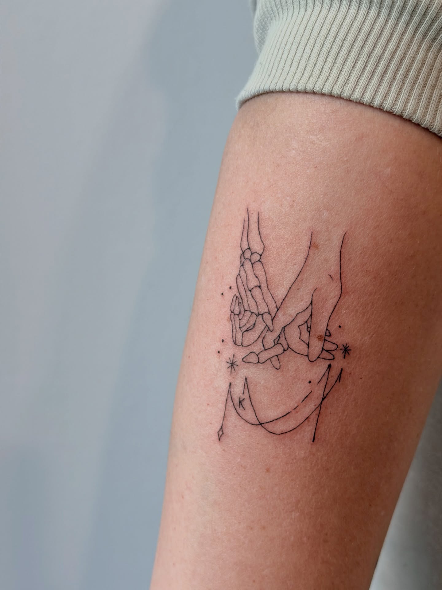 Hands and stars fine line tattoo on the forearm by Reverie Studio