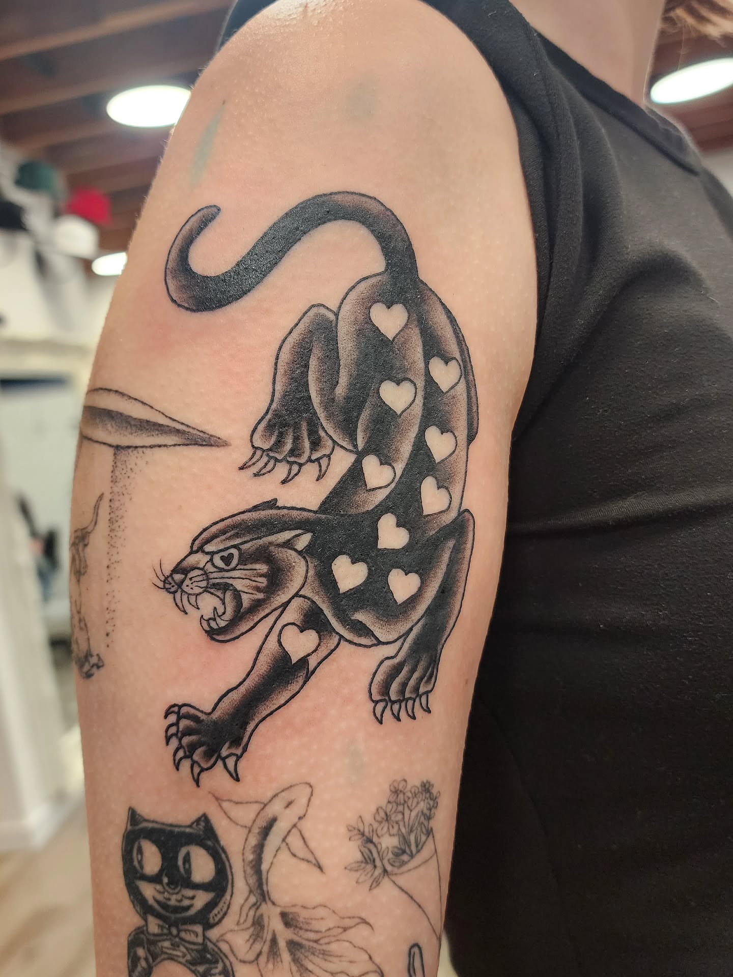 Panther with hearts black and grey tattoo on the upper arm by mikayla