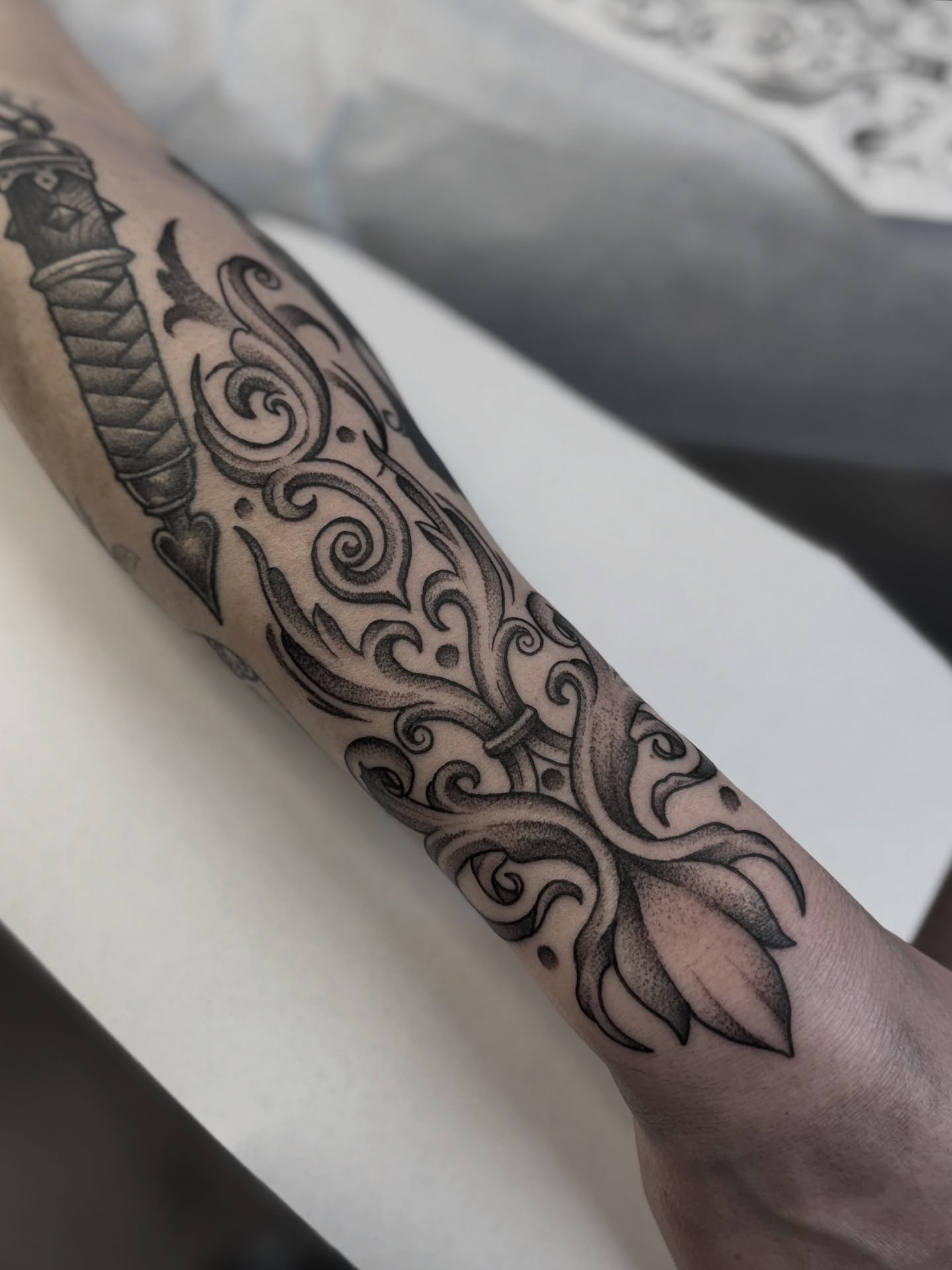 Knife and ornamental swirls ornamental tattoo on the forearm by Andrew