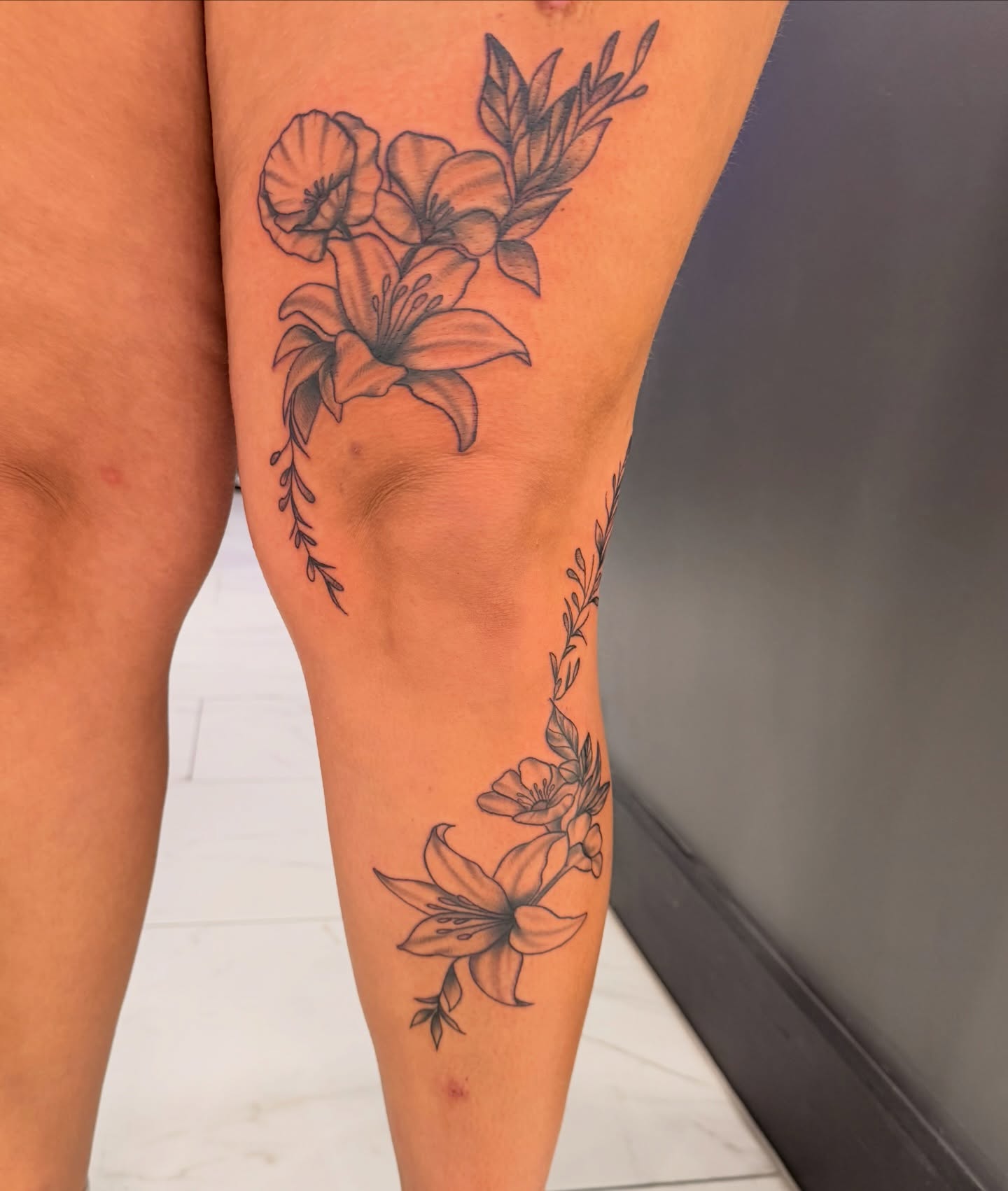 Lilies and leaves black and grey tattoo on the thigh by Lexi Odam