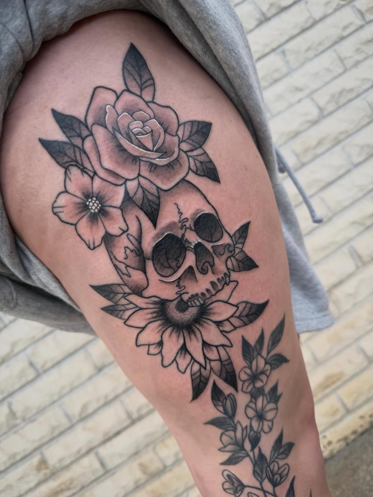 Skull and flowers black and grey tattoo on the thigh by Abby Hofman