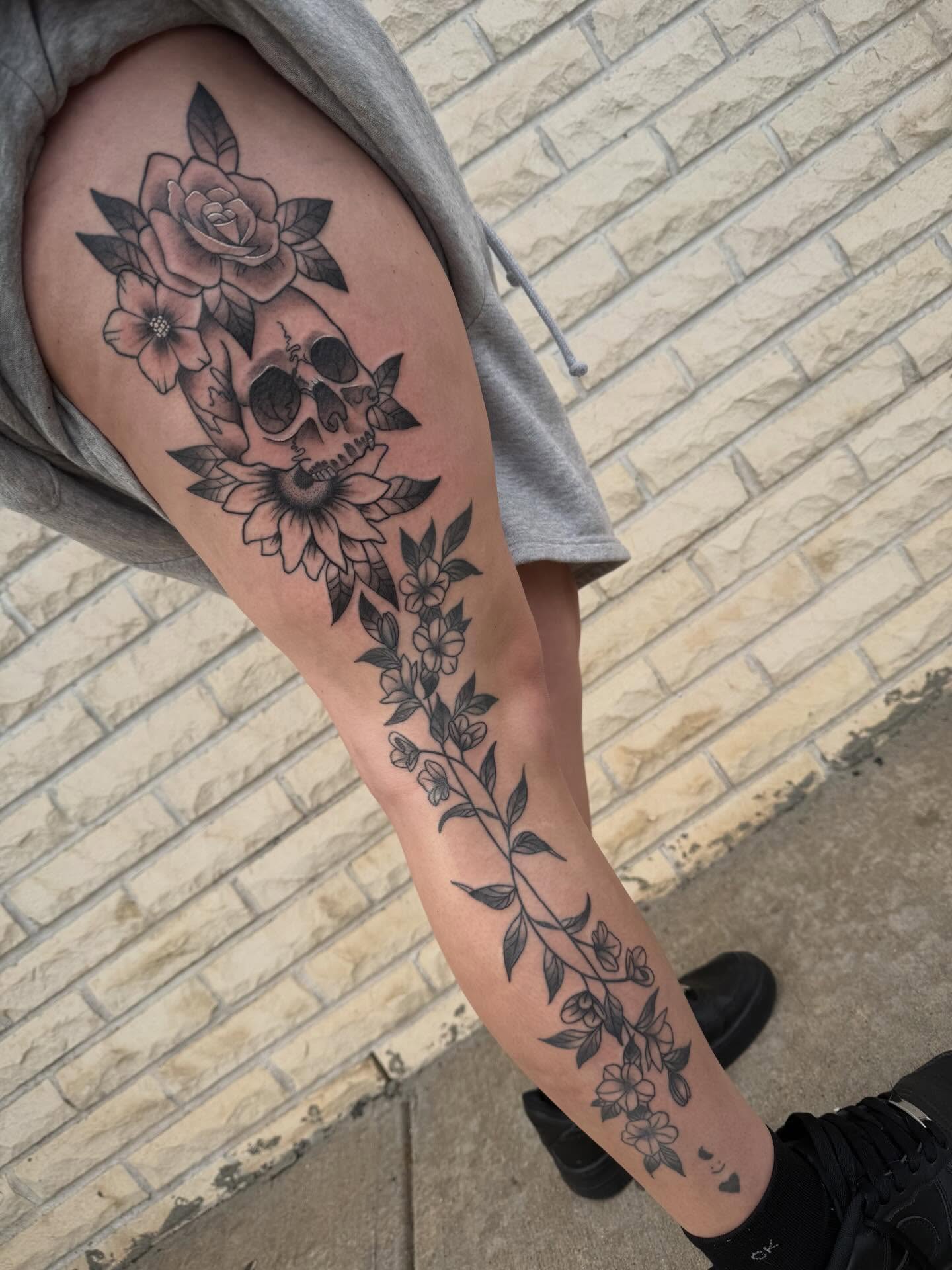 Skull and floral black and grey tattoo on the thigh by Abby Hofman
