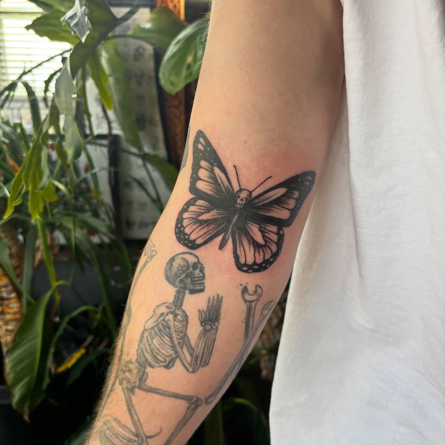 Butterfly and skeleton black and grey tattoo on the forearm by Lilly Evans