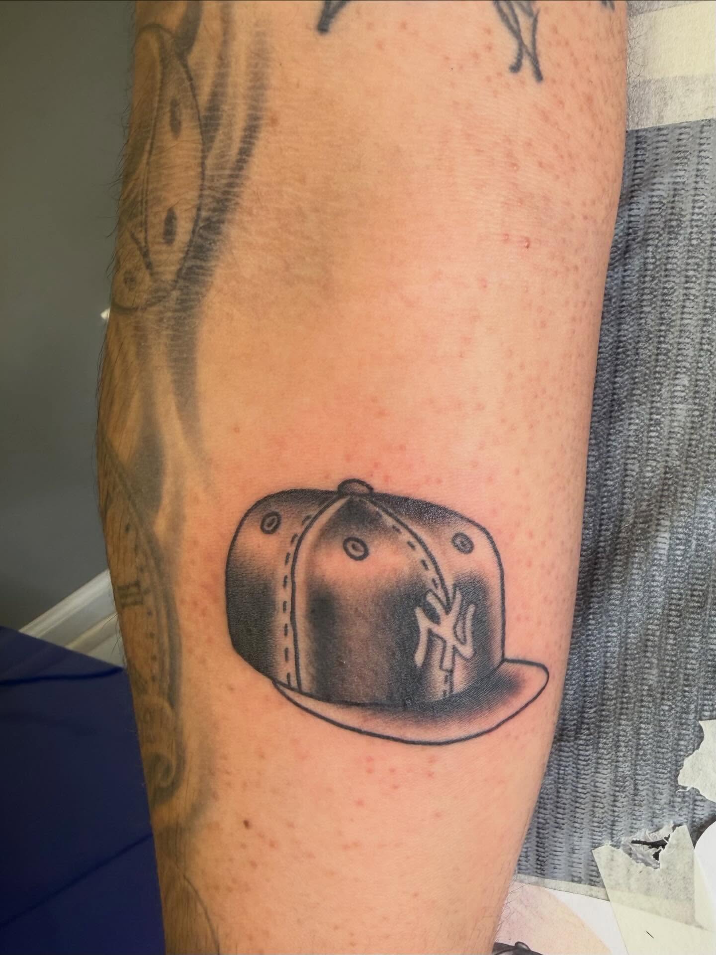 Ny cap black and grey tattoo on the forearm by linda perez