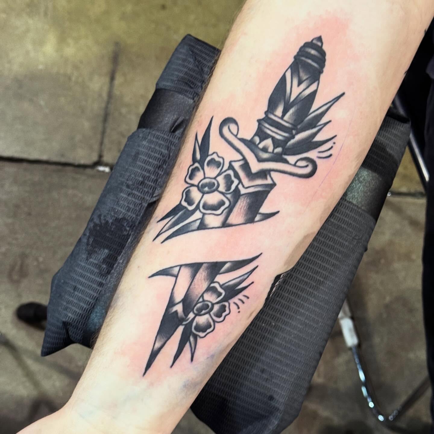 Crossed swords and flowers black and grey tattoo on the forearm by Jack Hatchet Tattoos