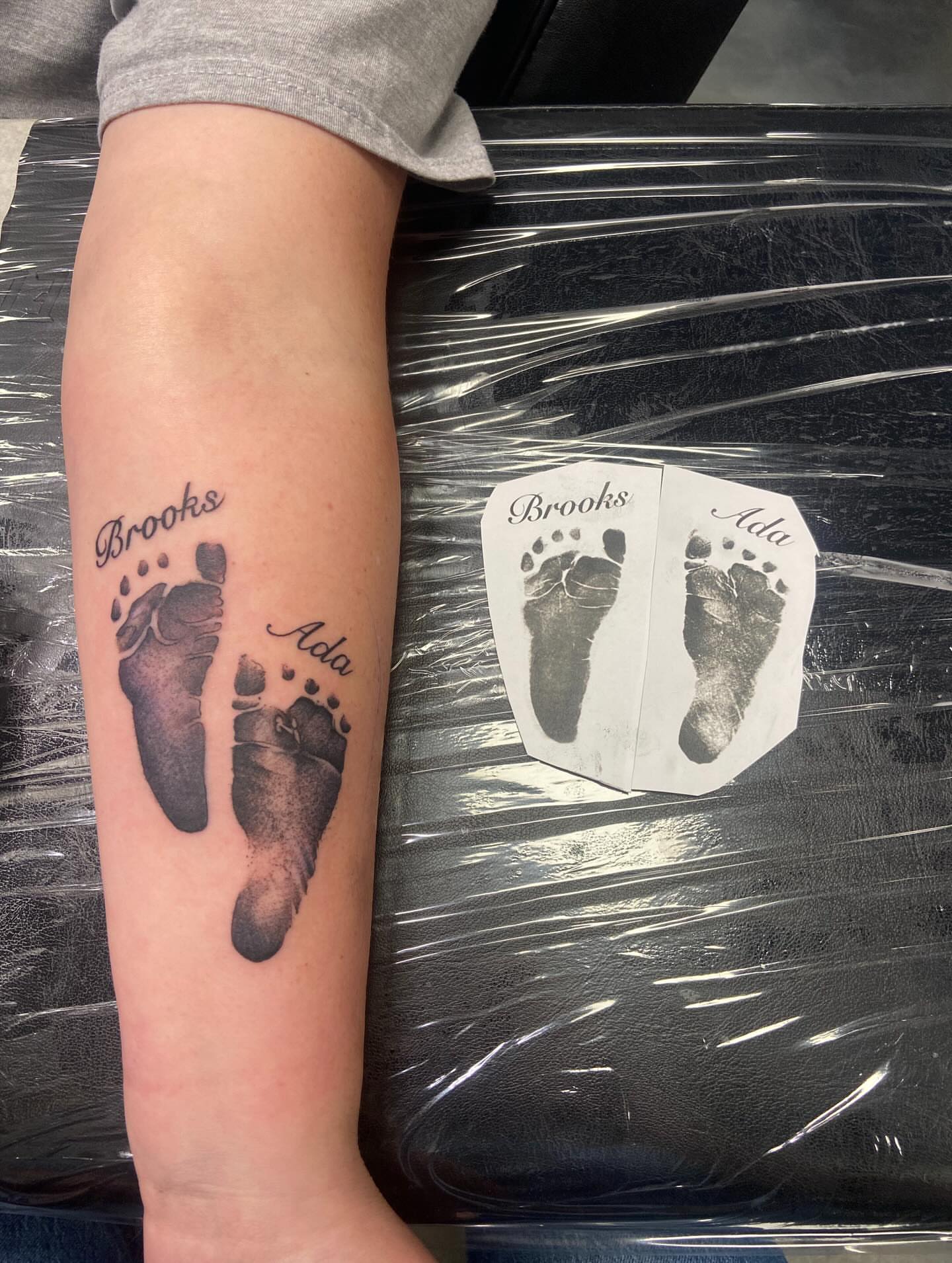 Baby footprints black and grey tattoo on the forearm by Sam Hearnen, Lawrence, Kansas