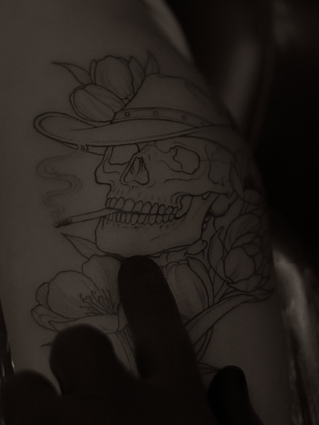 Skull with hat and flowers black and grey tattoo on the upper arm by Arthur Kossoski