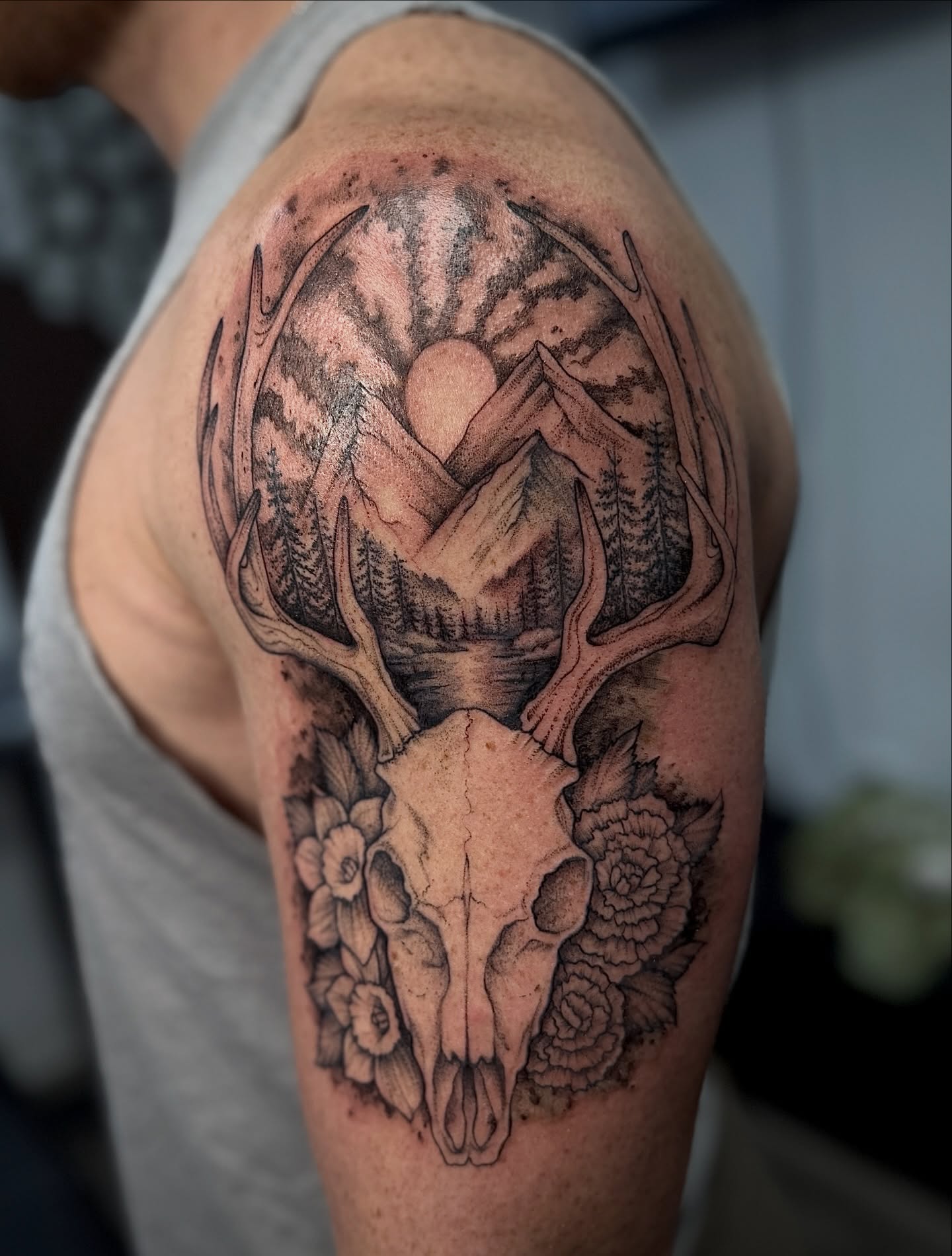 Deer skull and mountain landscape realism tattoo on the shoulder by 𝐀𝐝𝐫𝐢𝐞𝐥 𝐓𝐢𝐧𝐤𝐥𝐞𝐧𝐛𝐞𝐫𝐠 ⏾, Denison, Iowa