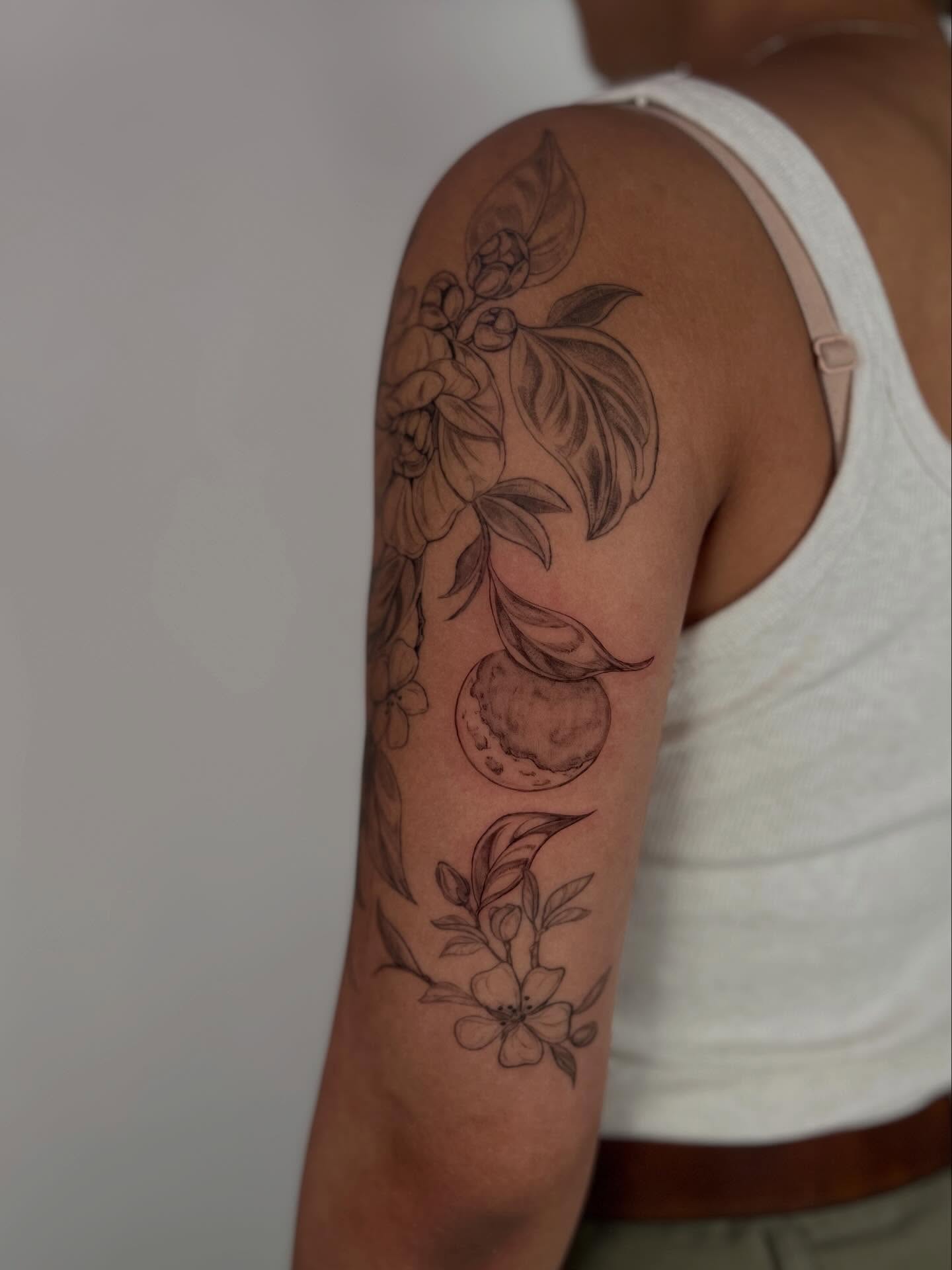 Fruit and floral black and grey tattoo on the upper arm by Sierra Skye