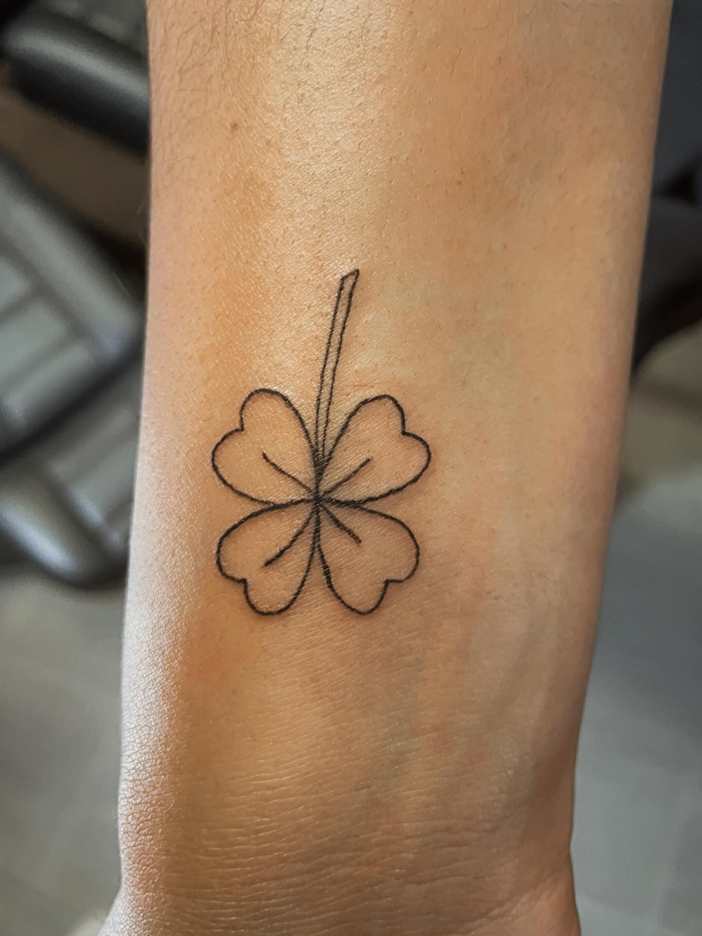 Four-leaf clover black and grey tattoo on the forearm by 𝚃𝙰𝚃𝚃𝙾𝙾 𝙰𝚁𝚃𝙸𝚂𝚃, Charlotte, North Carolina