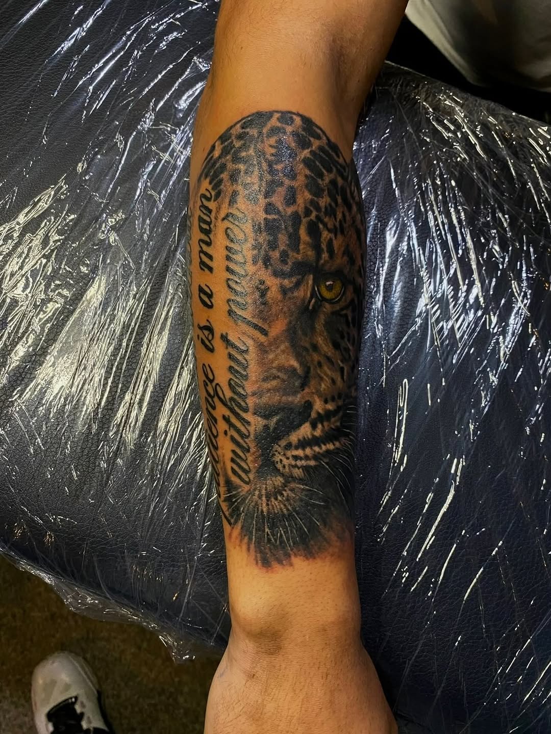 Leopard face with quote realism tattoo on the forearm by Jelani