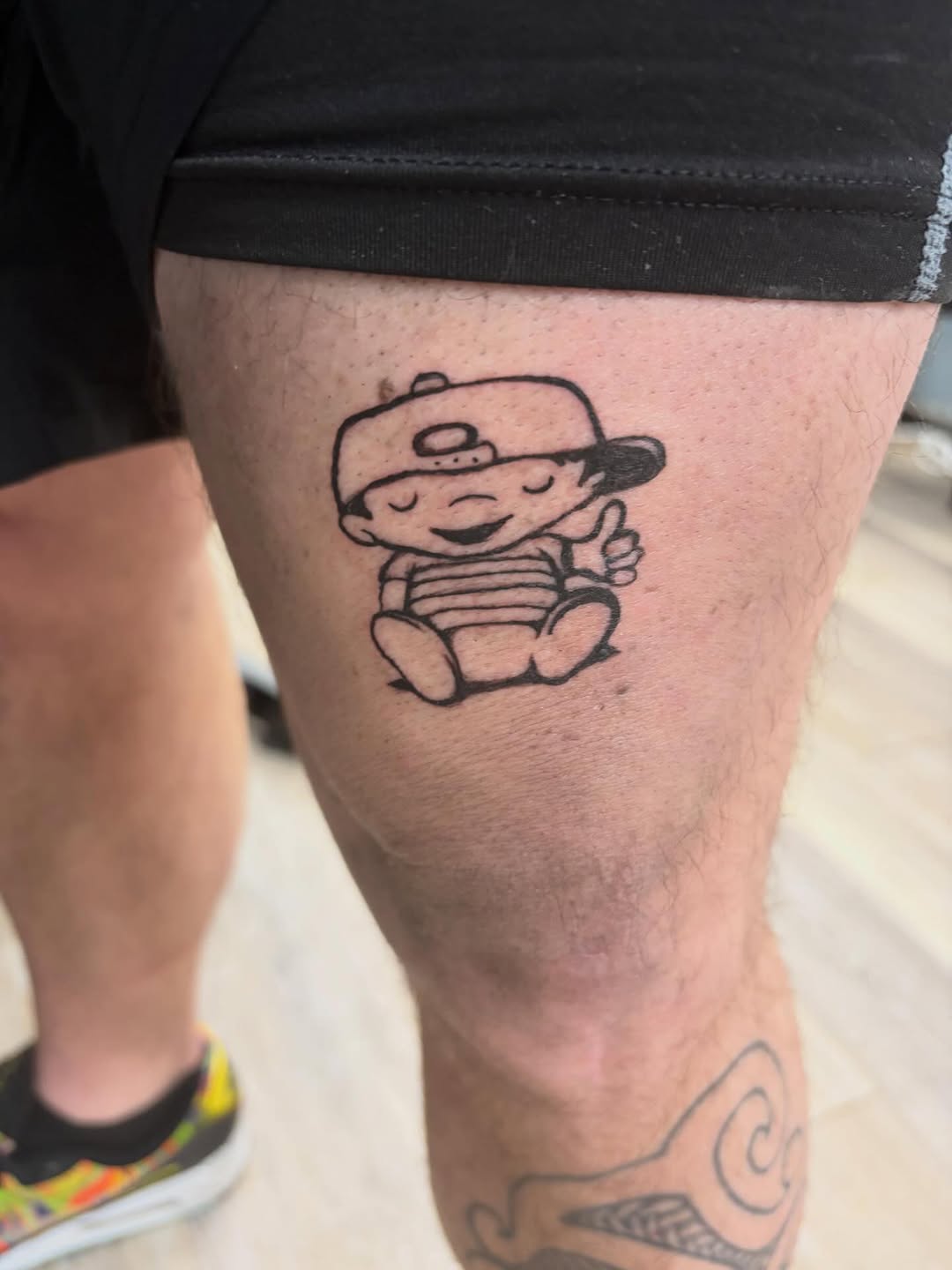 Cartoon character with cap tattoo on the thigh by Madison