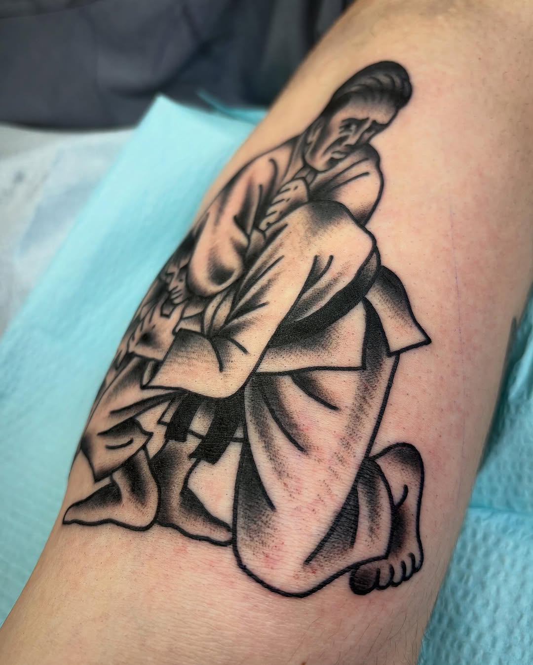 Two people grappling realism tattoo on the upper arm by Tom Wenzell