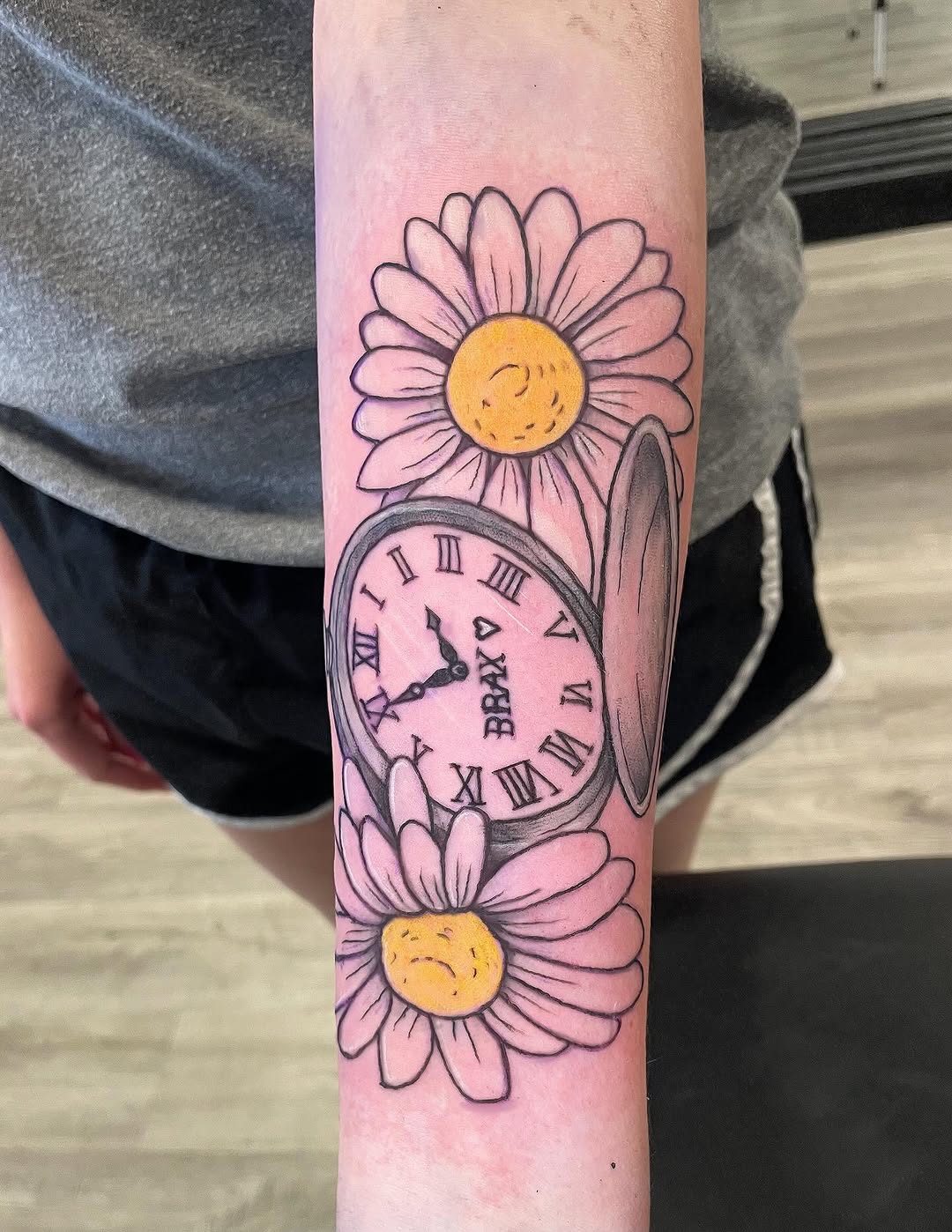 Pocket watch and daisies ignorant tattoo on the forearm by Logan Casimir