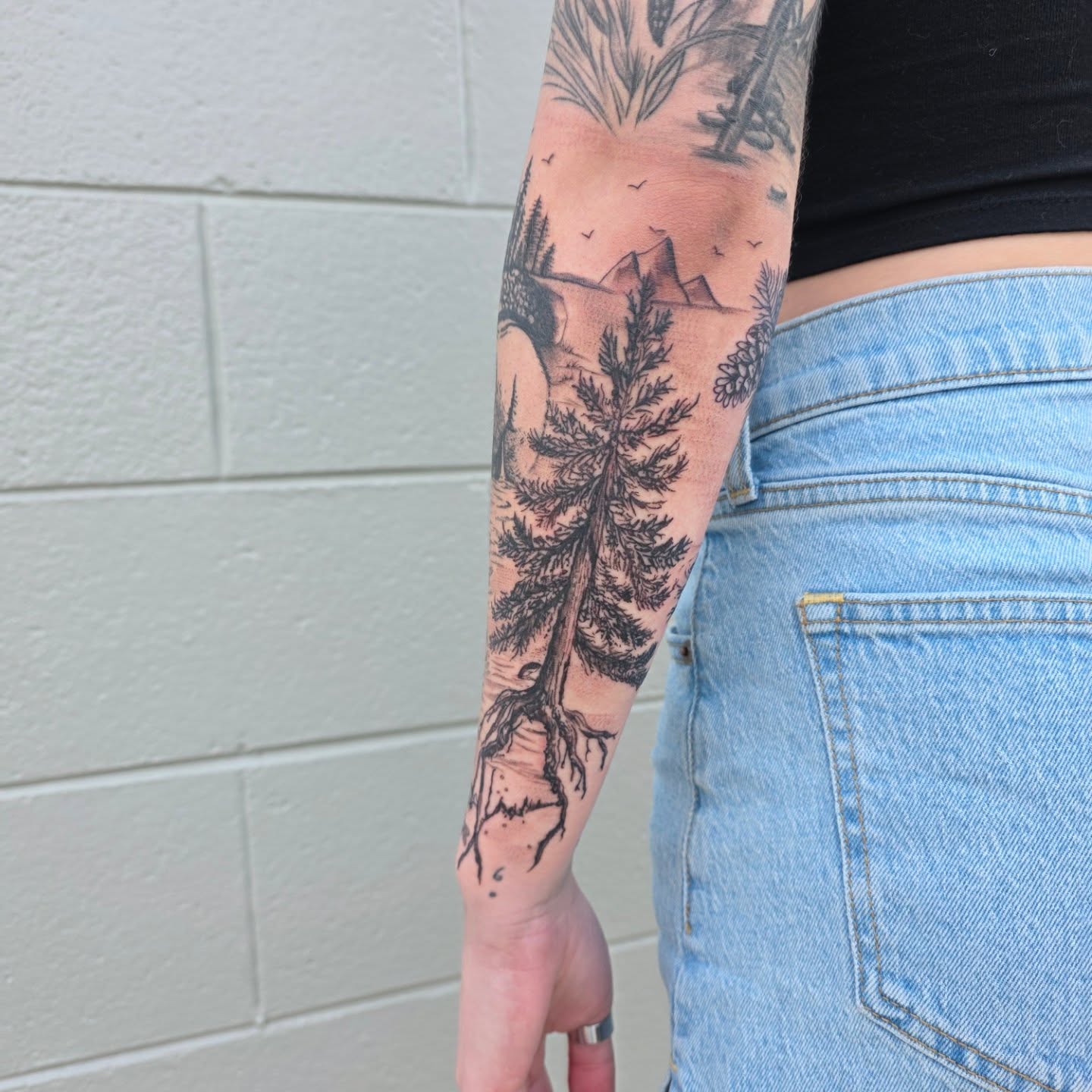 Pine tree landscape realism tattoo on the forearm by Maggie