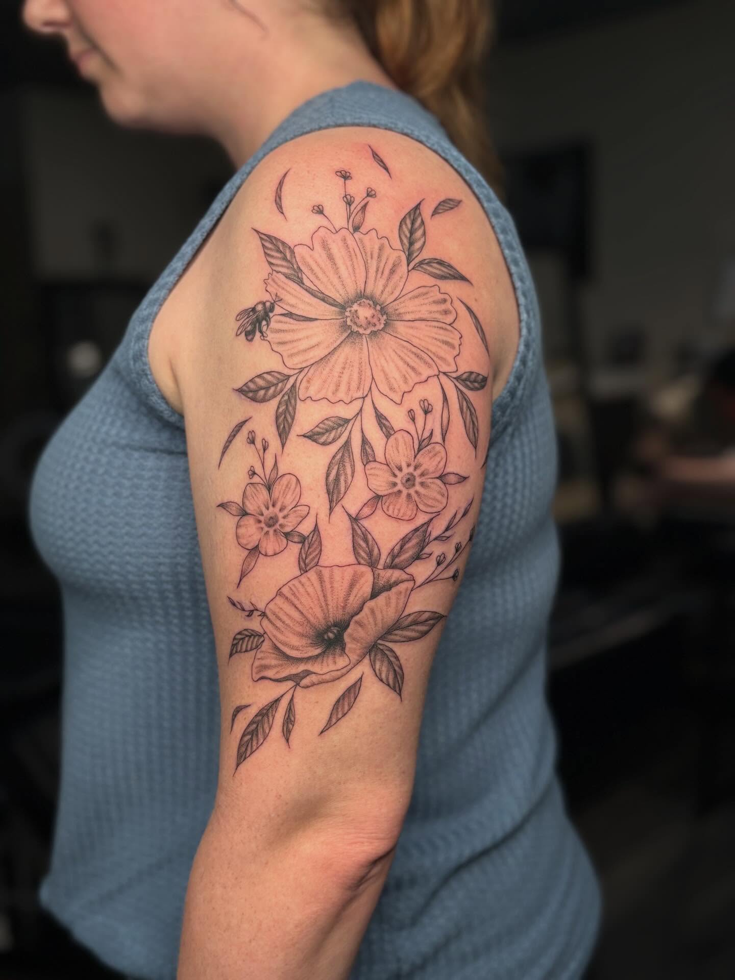 Floral arrangement black and grey tattoo on the upper arm by Tessa Simmons - Tattoo Artist