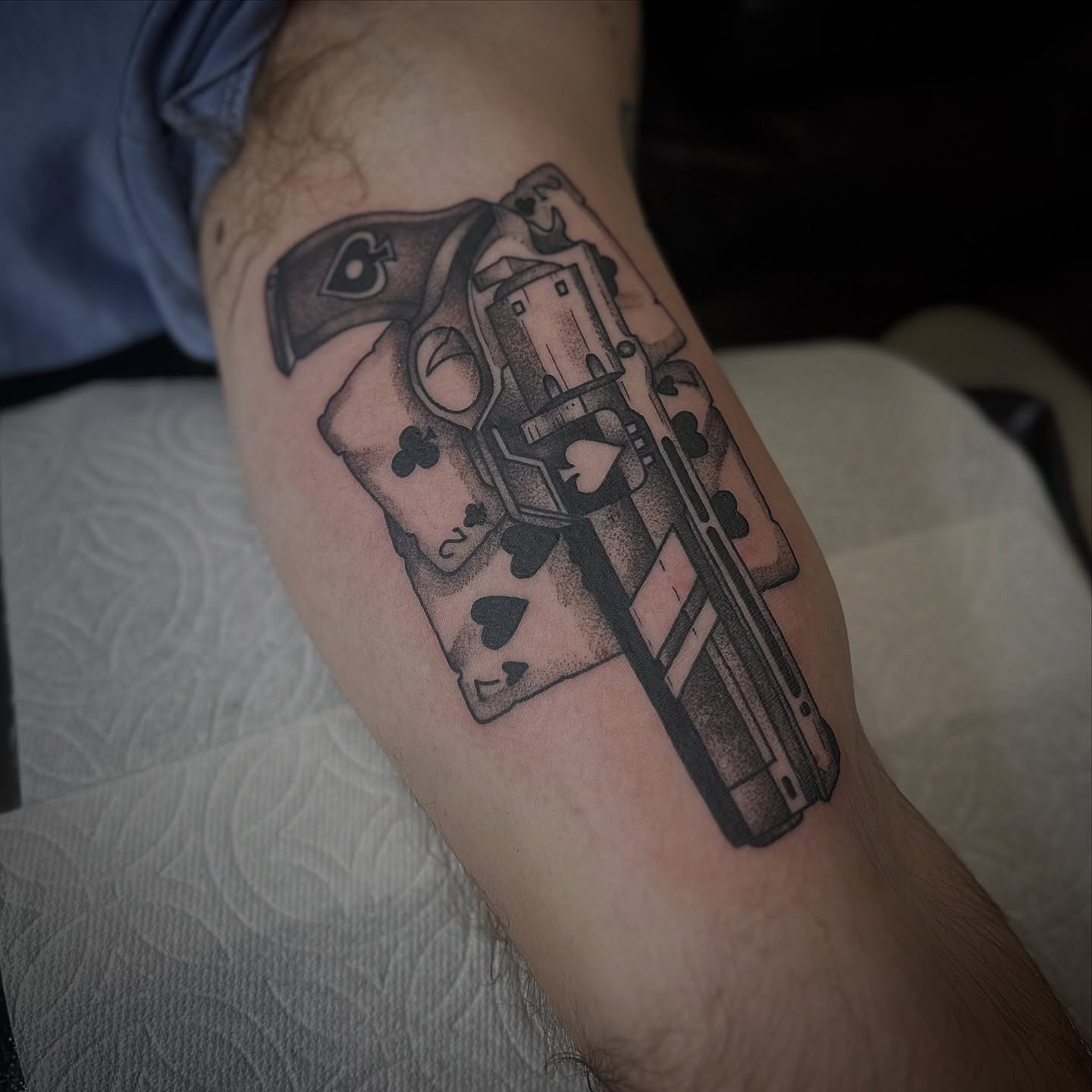 Gun and playing cards black and grey tattoo on the forearm by Walk-in American Traditional Tattoos Las