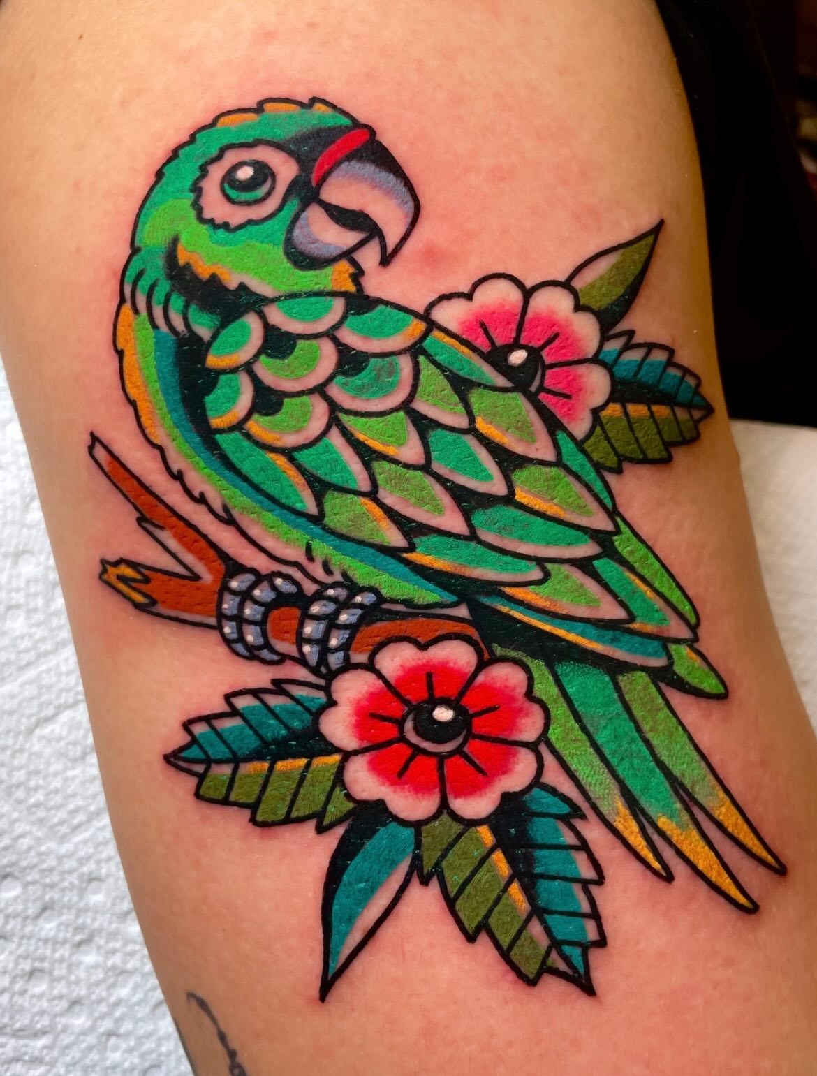 Parrot and flowers American traditional tattoo on the thigh by Ryan McDonald