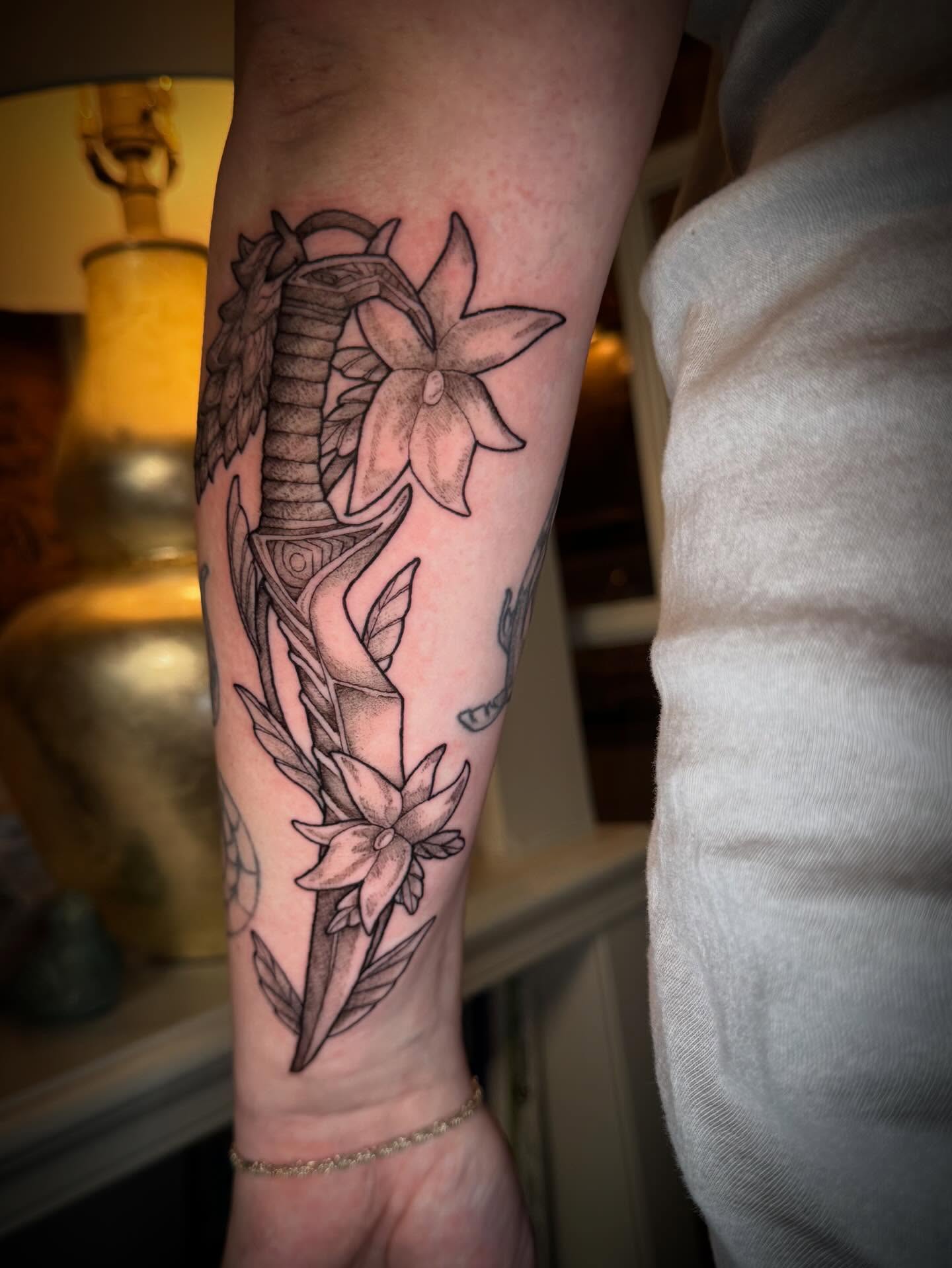Daffodil and sword black and grey tattoo on the forearm by Tattoos by Alex
