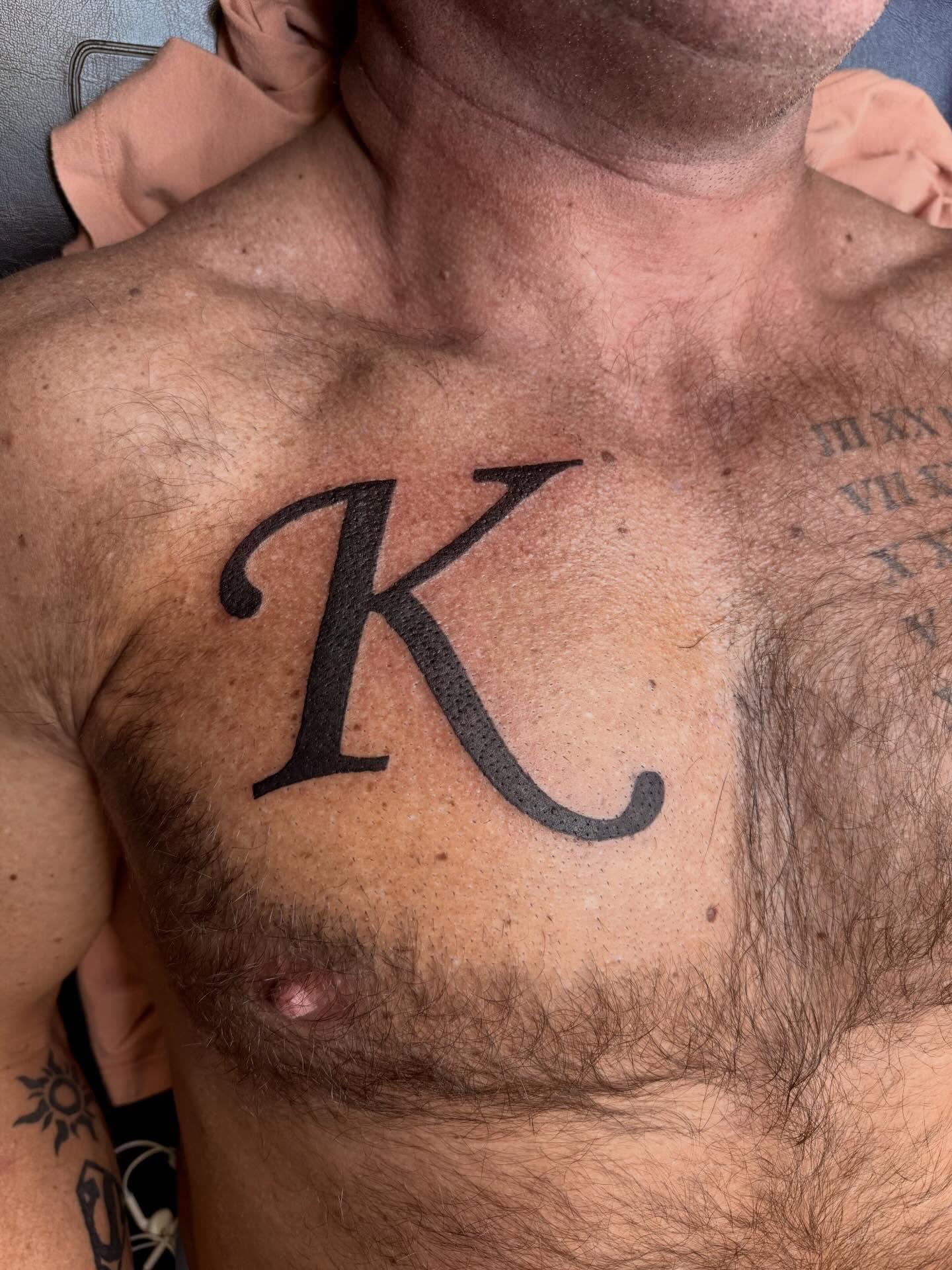 Letter K lettering script tattoo on the chest by ♱ C ♱, Dallas, Texas