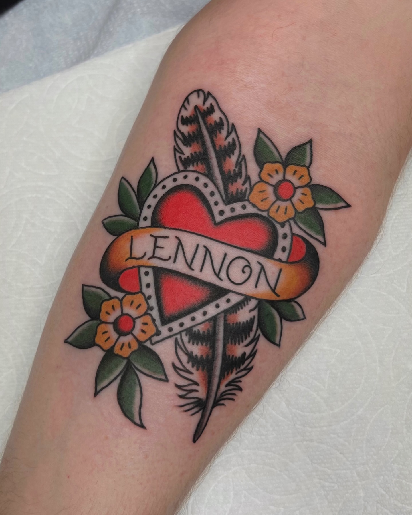 Heart with feather and flowers American traditional tattoo on the forearm by Brian Visser