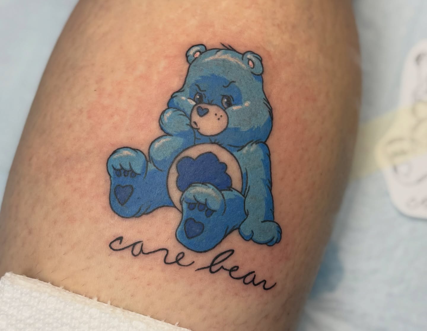 Blue care bear illustrative tattoo on the thigh by Minxxy Tattoos