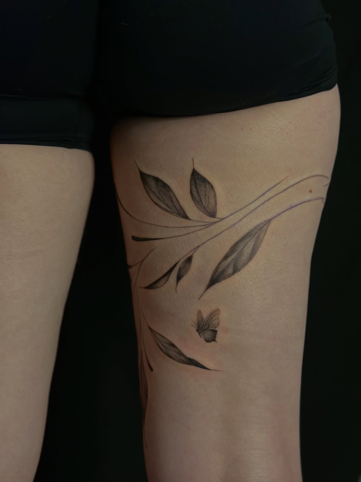Leaves and butterfly black and grey tattoo on the thigh by Tattoo artist Denver