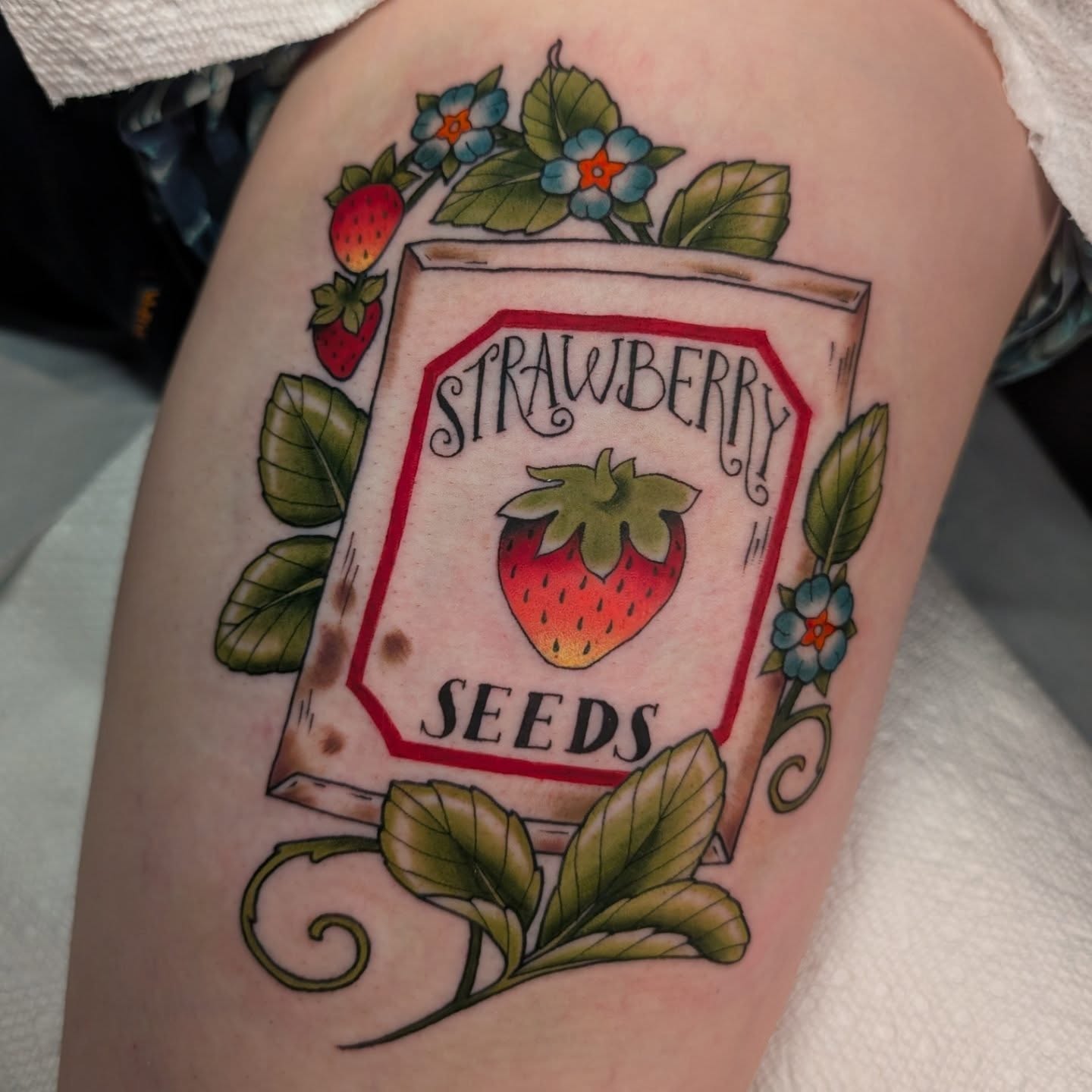 Strawberry seed packet American traditional tattoo on the thigh by Ellie