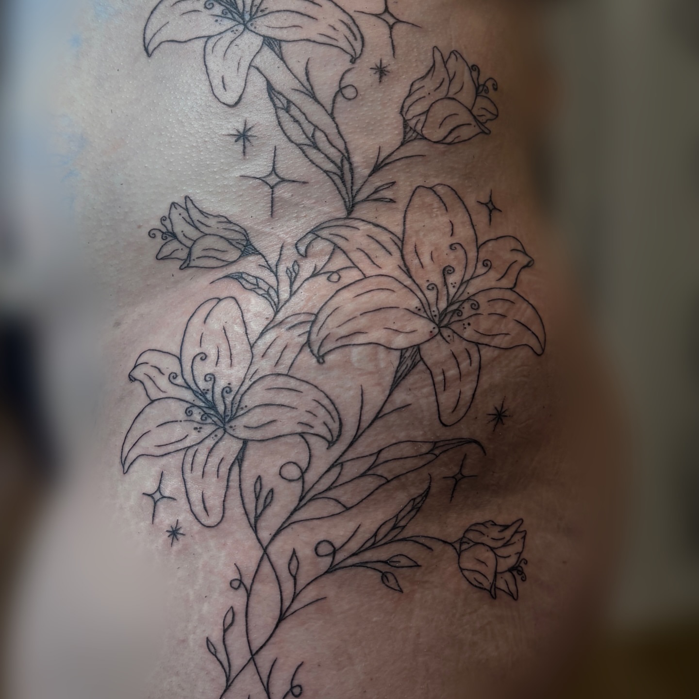 Lilies and stars black and grey tattoo on the upper arm by Emma🌸✨Austin Tattoo Artist