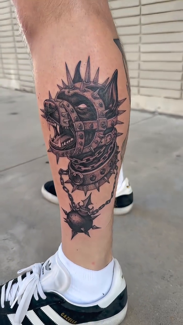 Dog head with spikes and chains realism tattoo on the leg by Michael Bogle