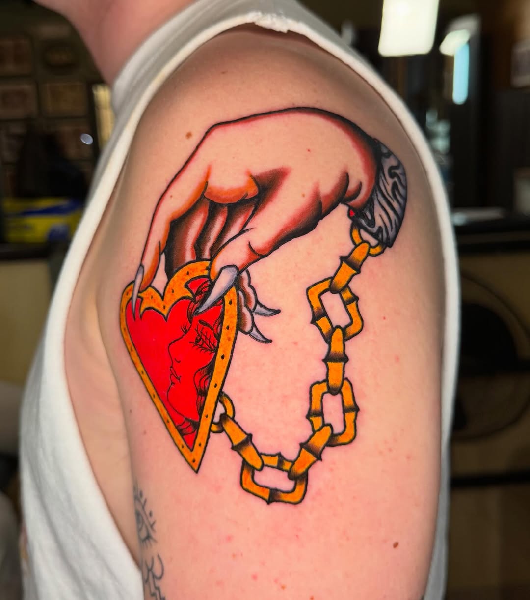 Hand holding a heart locket neo-traditional tattoo on the shoulder by @michaelryan_tattoo