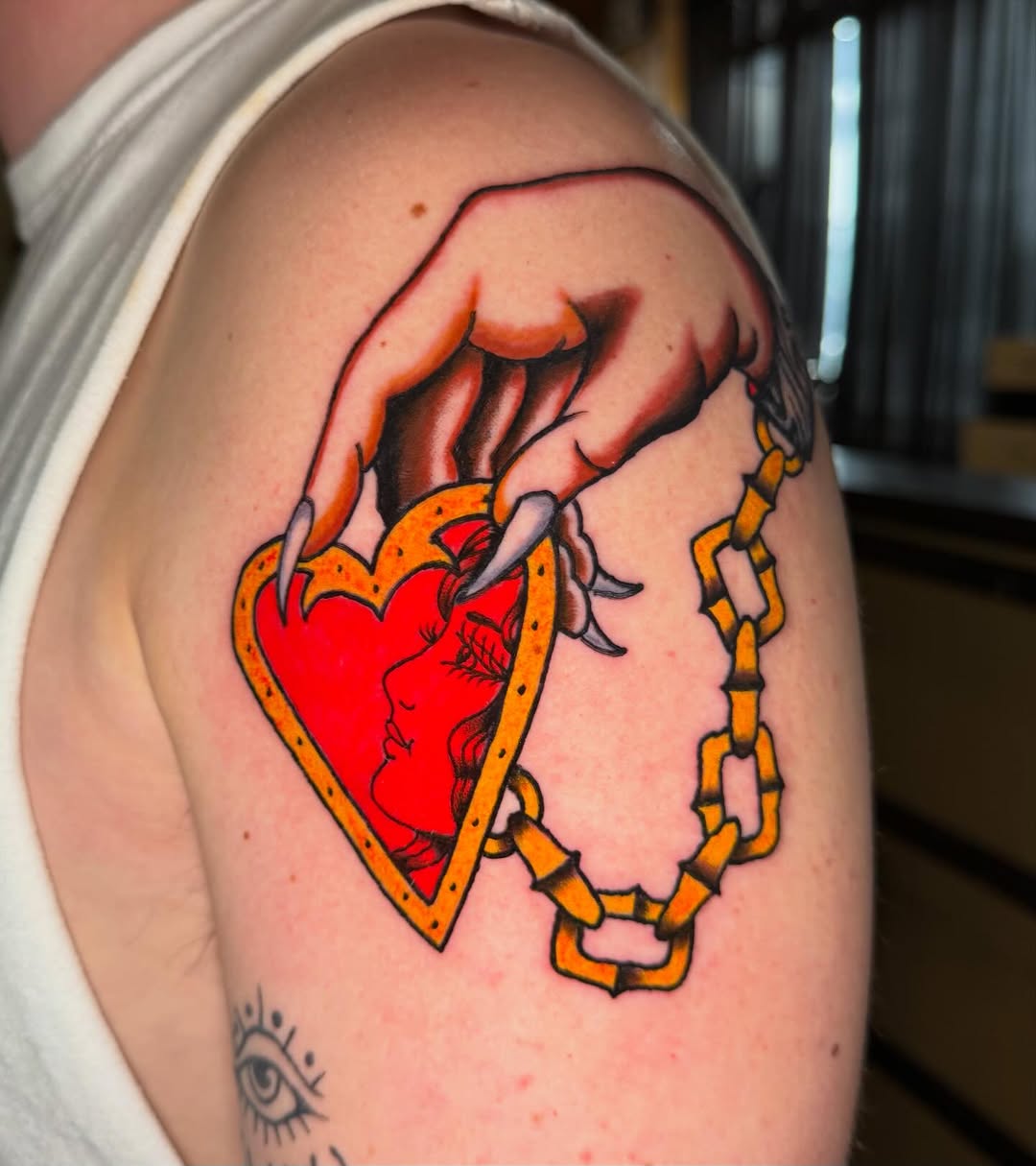 Heart with profile and chain American traditional tattoo on the shoulder by @michaelryan_tattoo