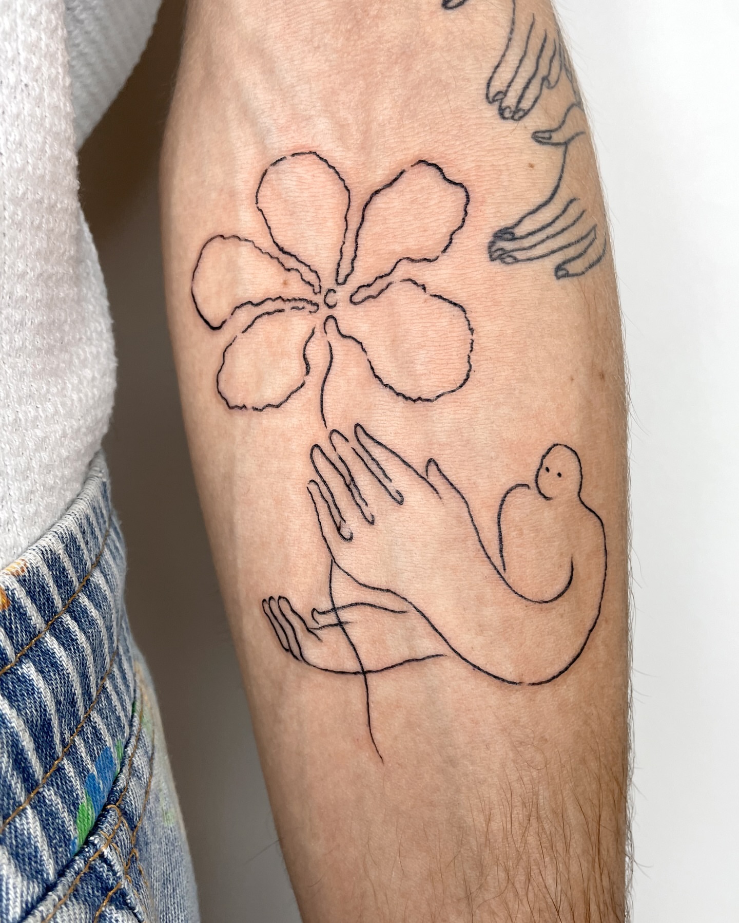 Flower and hands minimalist tattoo on the forearm by Eden Kalif