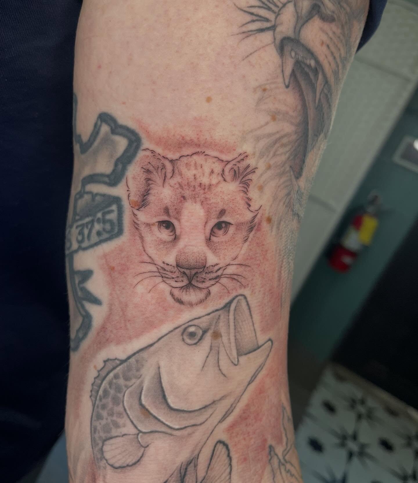 Lion cub and fish dotwork tattoo on the forearm by Allison Gallagher