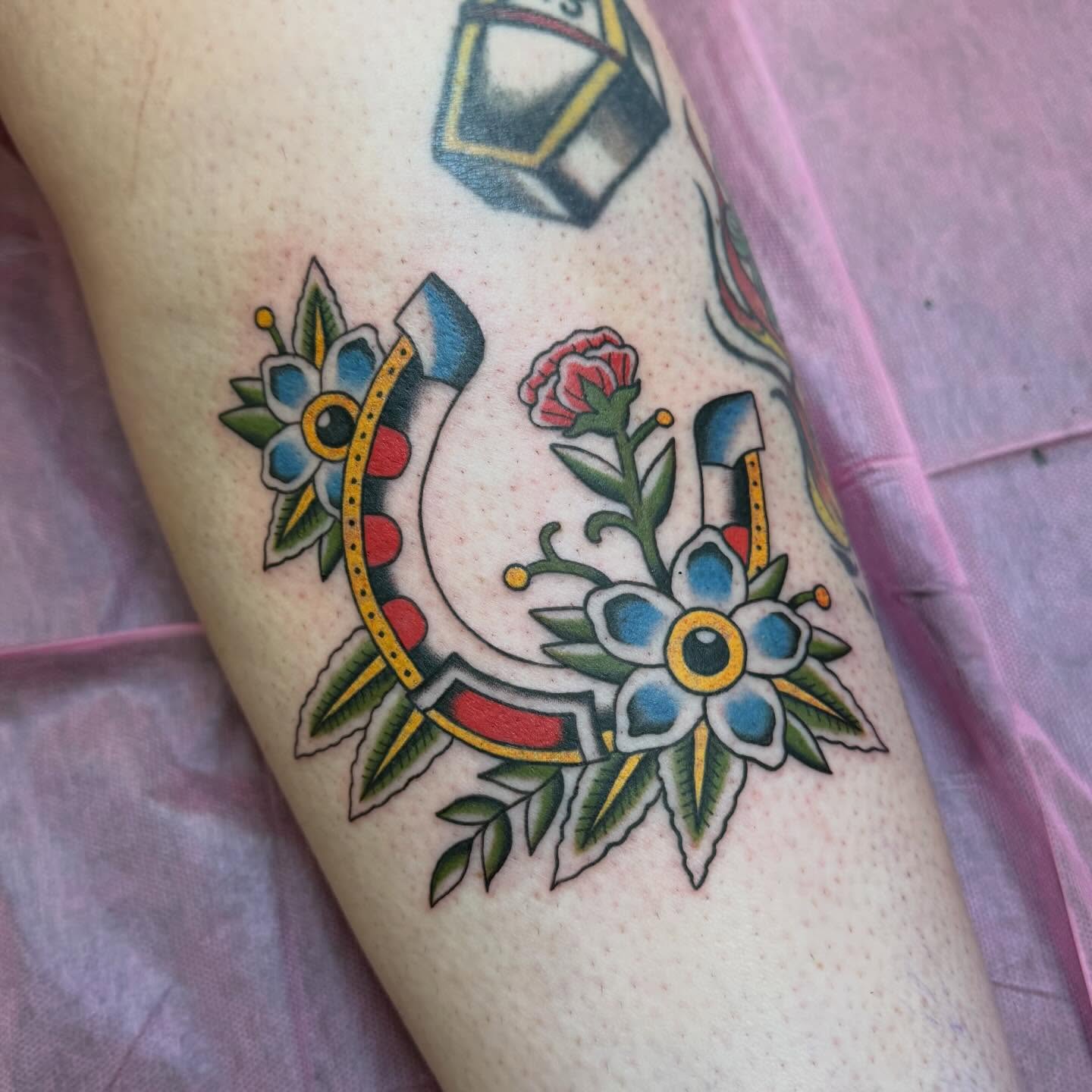 Horseshoe and flowers American traditional tattoo on the forearm by charlie