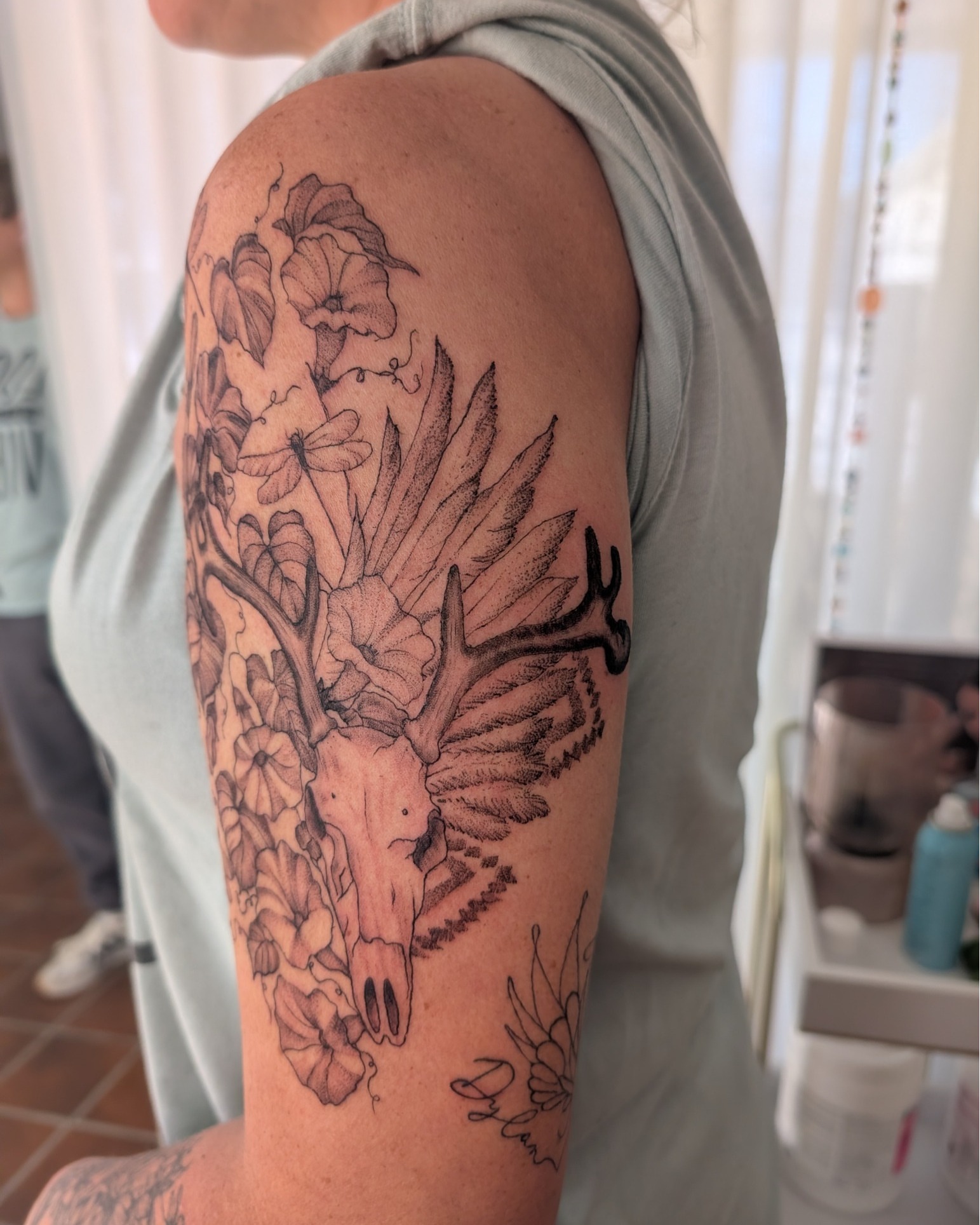 Deer skull with flowers realism tattoo on the upper arm by Arminda Walborn