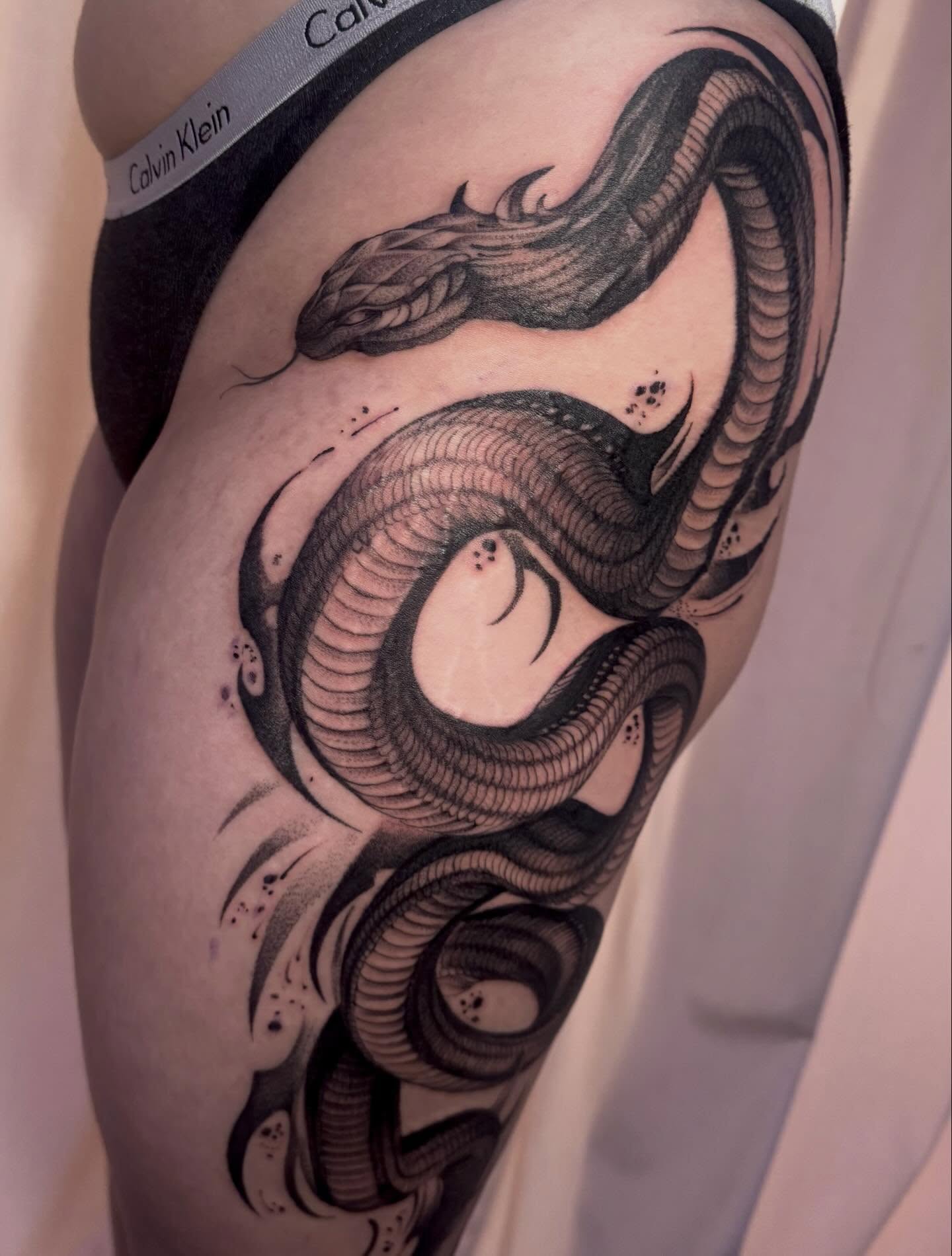 Snake black and grey tattoo on the thigh by Claire Litsey