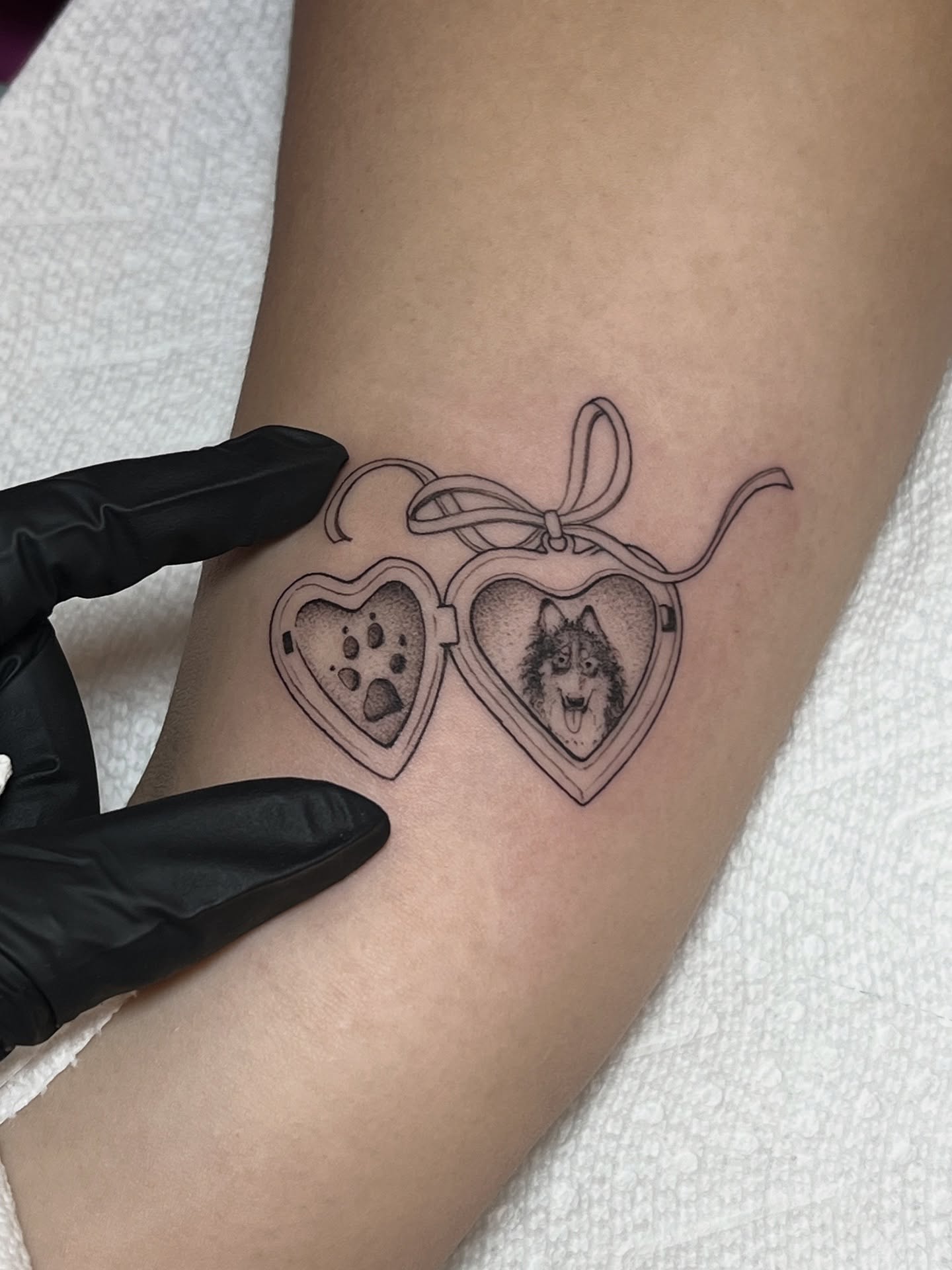 Locket with dog black and grey tattoo on the forearm by Tehnaya