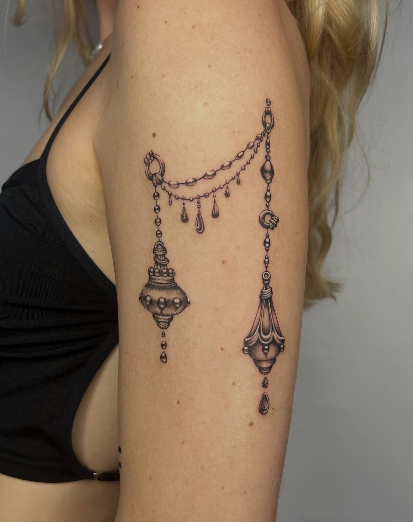 Chandelier black and grey tattoo on the upper arm by Lauren ๐