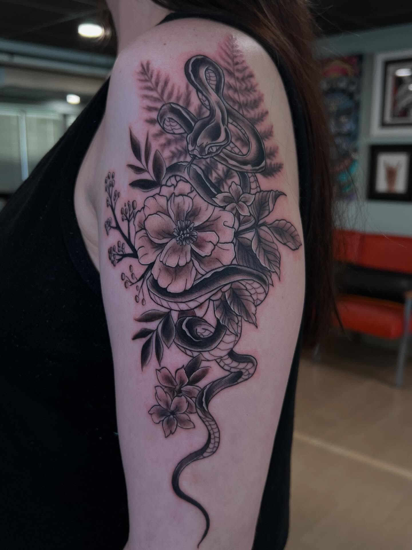 Snake and flowers black and grey tattoo on the upper arm by Jessica Kloos