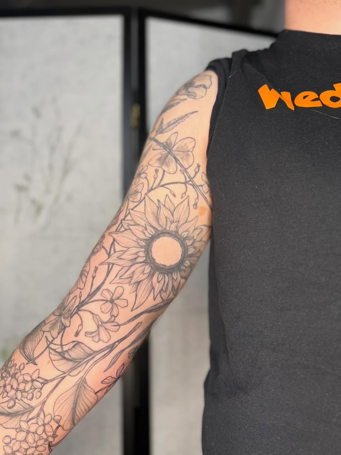 Sunflower and floral black and grey tattoo on the forearm by Noelle Adrienne Tattoos