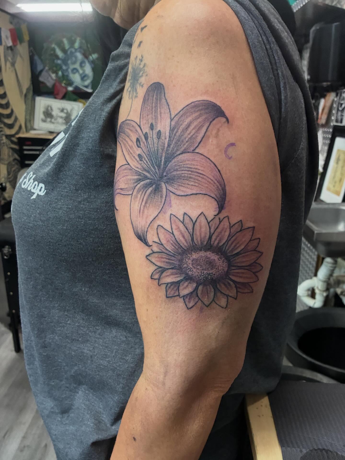 Lily and sunflower realism tattoo on the upper arm by Trae