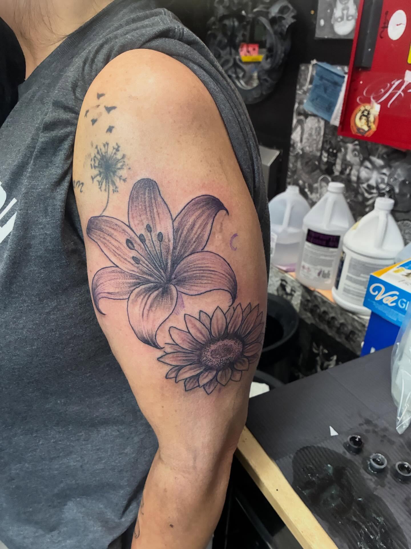 Lily and sunflower realism tattoo on the upper arm by Trae